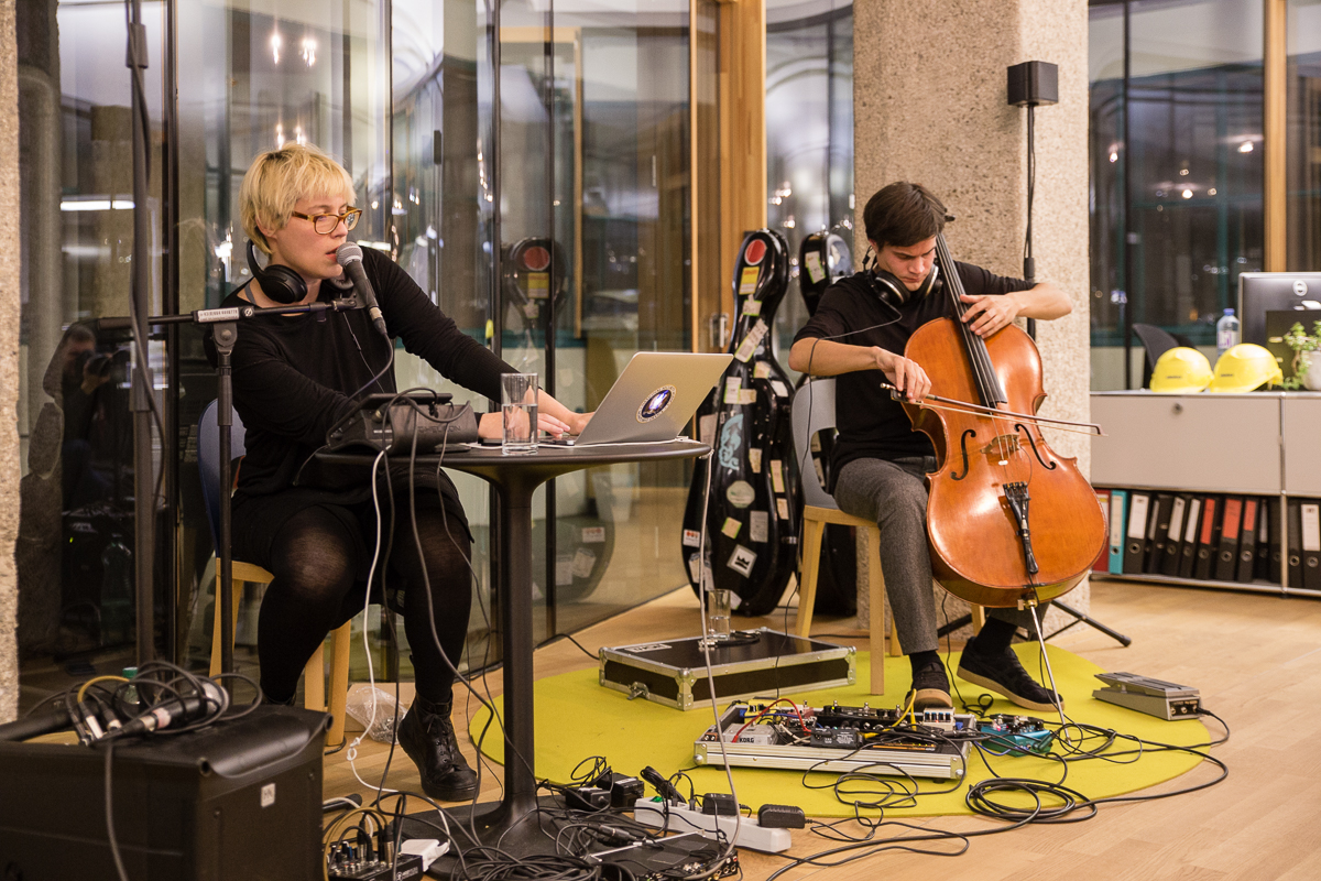 Eine Band spielt, eine Frau singt in ein Mikrofron und ein Mann spielt Cello.