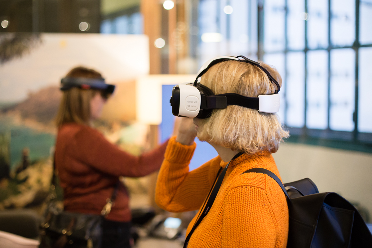 Eine Frau mit orangefarbenen Pullover trägt konzentriert eine VR Brille.