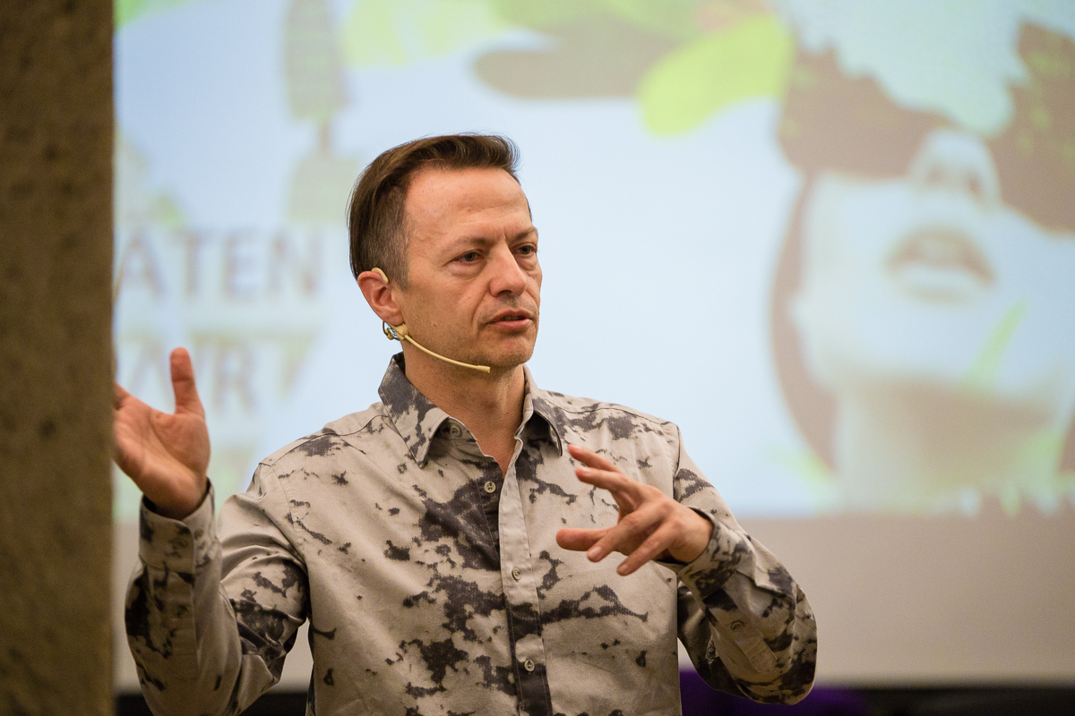 Ernst Demmel (Netural) mit Headset Mikrofon steht vor einer Leinwand mit Präsentation und spricht.