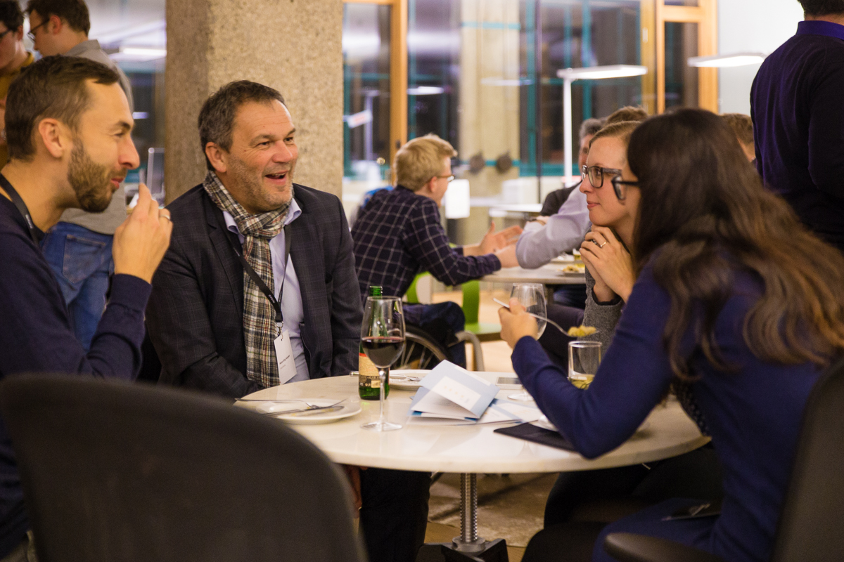 Vier Menschen sitzen um einen runden Tisch und unterhalten sich lachend.