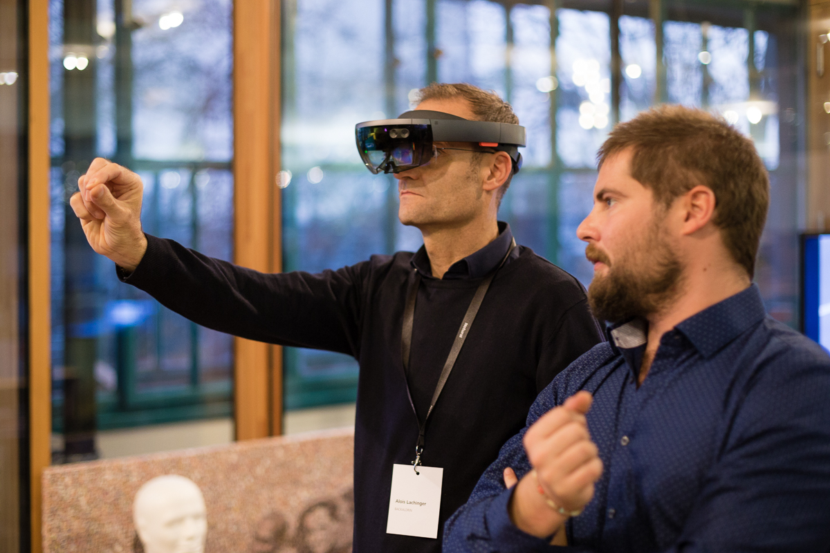 Ein Mann trägt eine VR-Brille und interagiert mit der virtuellen Umgebung, während ihm ein anderer zusieht.