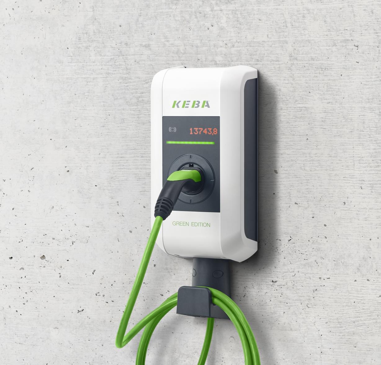 Weiße E-Ladestation mit grünem Ladekabel an einer Betonwand.