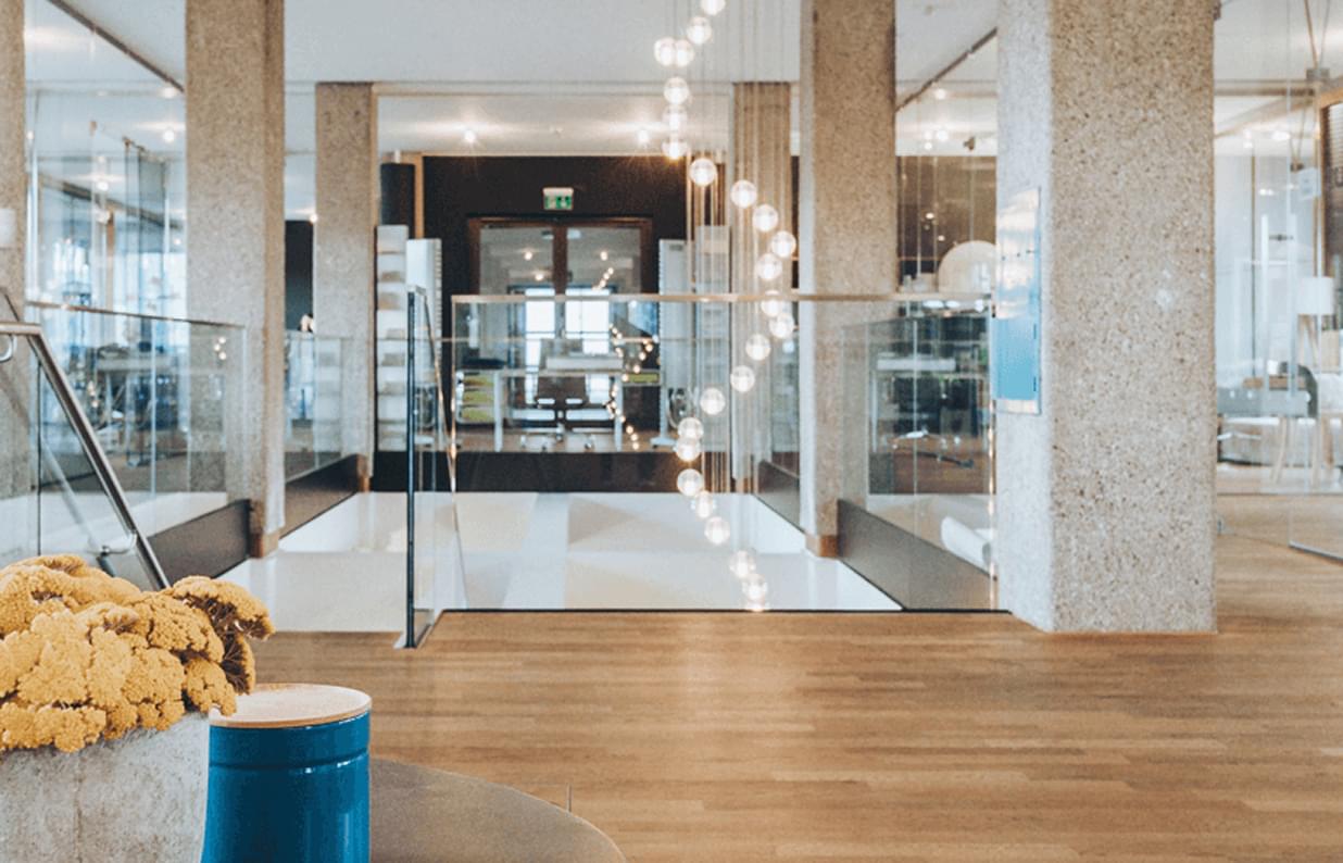 Modernes, offenes Büro mit Holzfußboden, Sichtbetonsäulen und einer dekorativen Lichterkette über einem Durchgang.