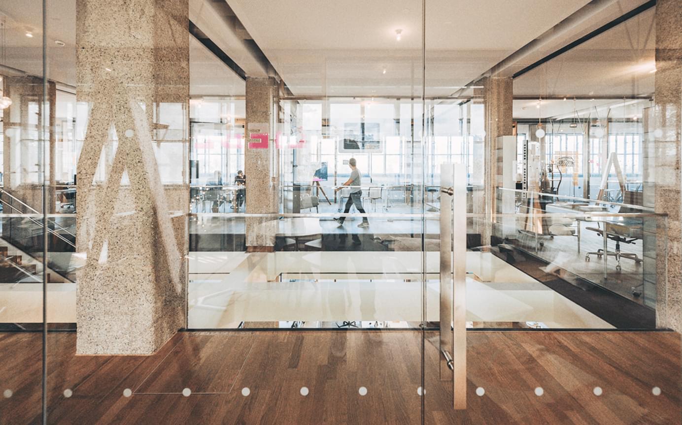 Blick durch die Glaswände eines hellen, modernen Büros mit Spiegelungen.