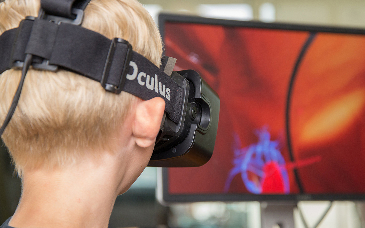 Junge Person mit Oculus VR-Brille betrachtet eine medizinische Simulation auf einem Monitor.