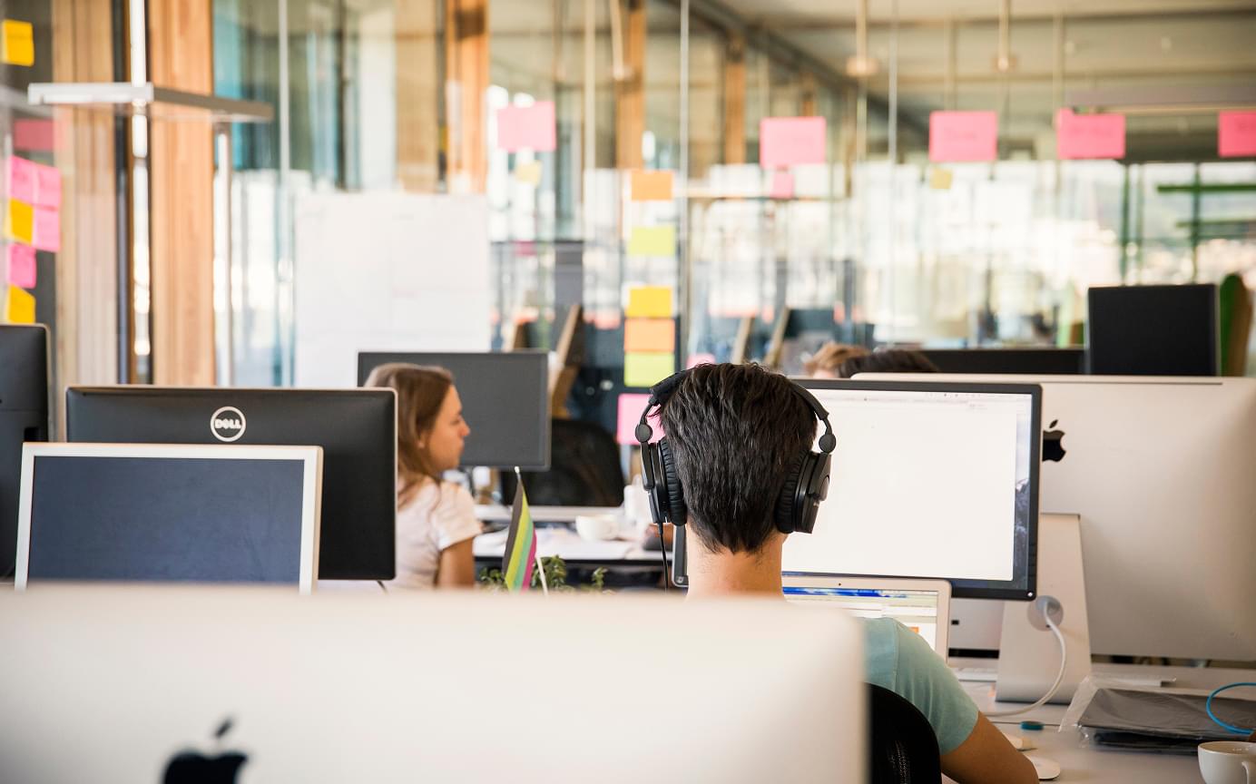 Mehrere Personen sitzen an einem Tisch mit Laptops, Post-its, Stiften und unterhalten sich während eines Workshops.