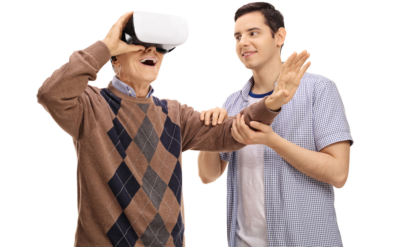 Älterer Mann erlebt mit Unterstützung eines jungen Mannes Virtual Reality mit VR-Brille.