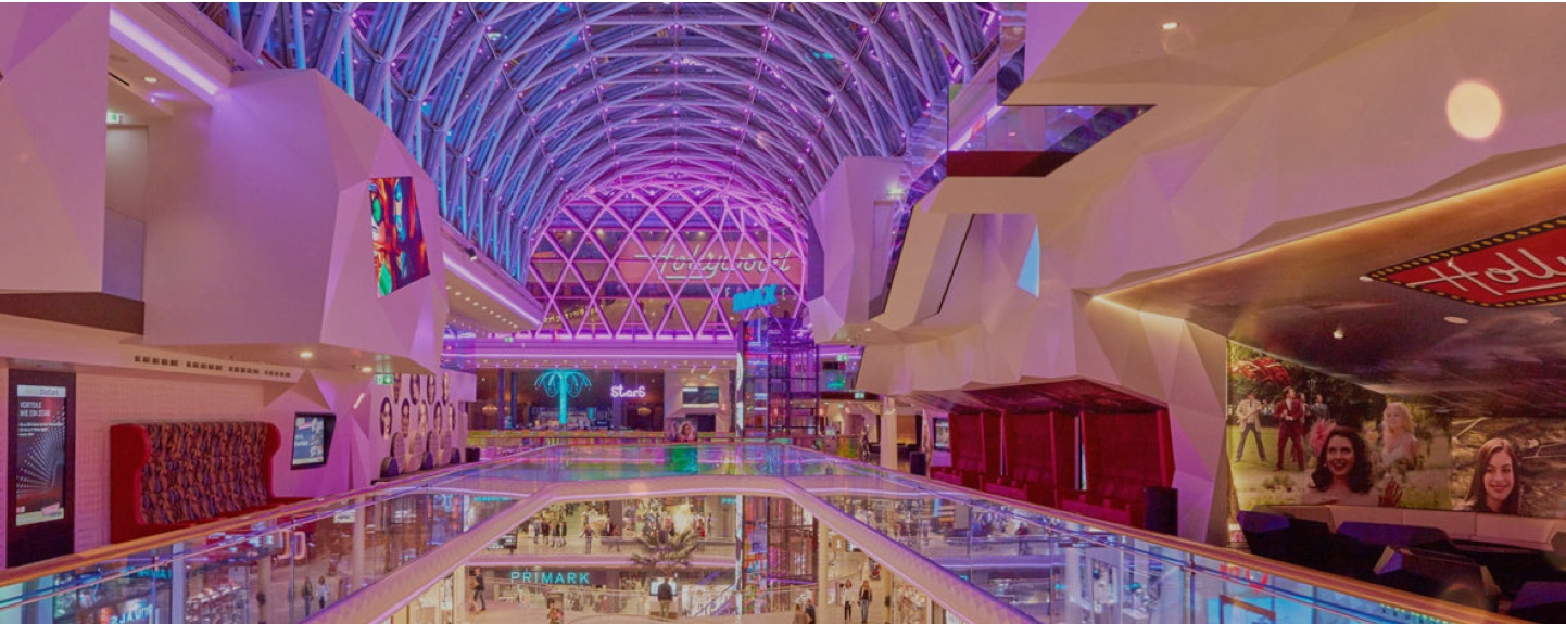 Innenansicht der PlusCity mit leuchtendem, futuristischem Design, Shops und Kinozugang.