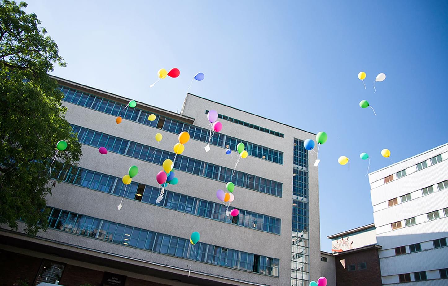 Außenansicht der Tabakfabrik Linz mit bunten fliegenden Luftballons davor.