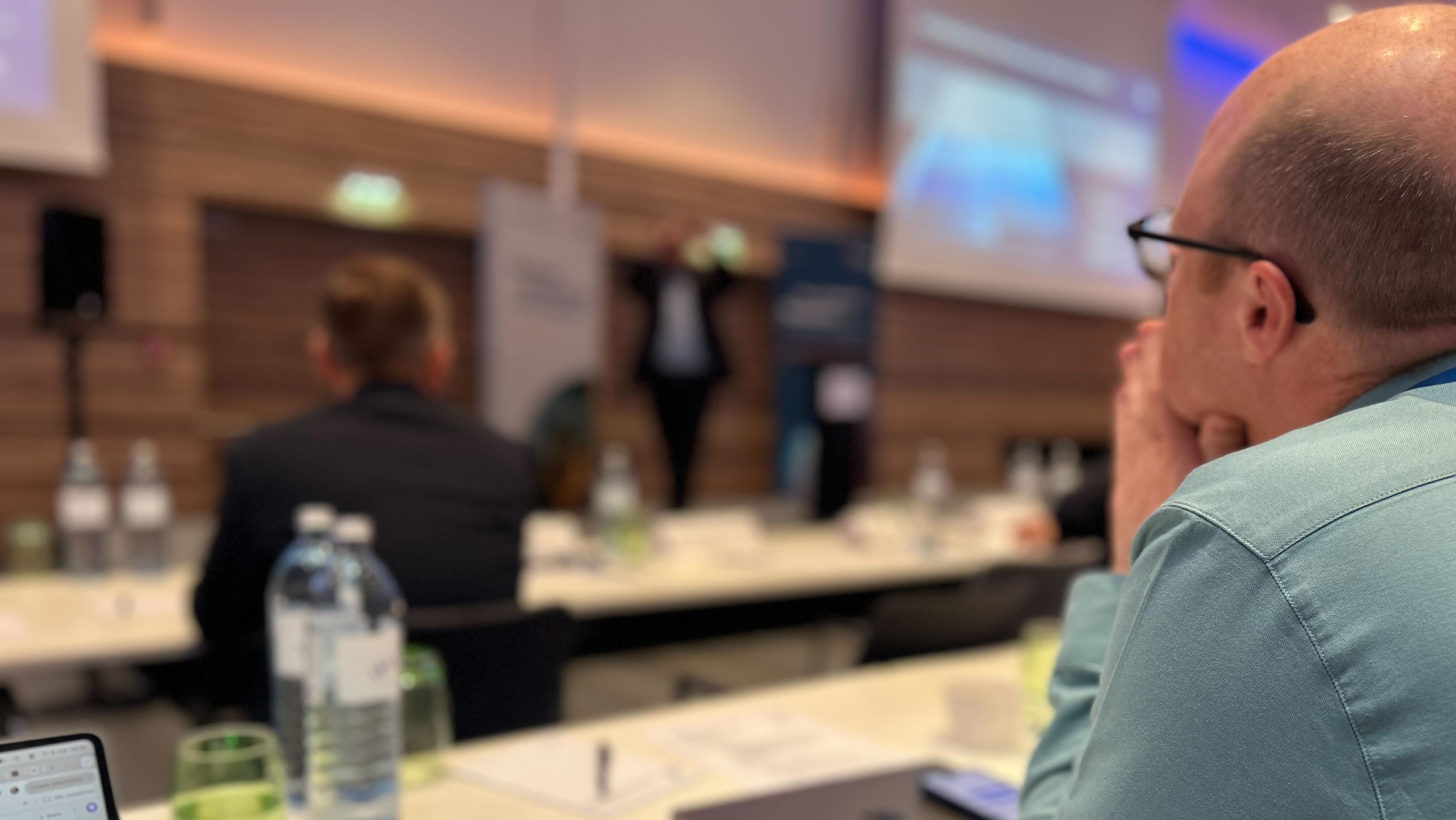 Norbert Täubl (Netural) hört im Vordergrund aufmerksam einem Vortrag auf der Bühne zu