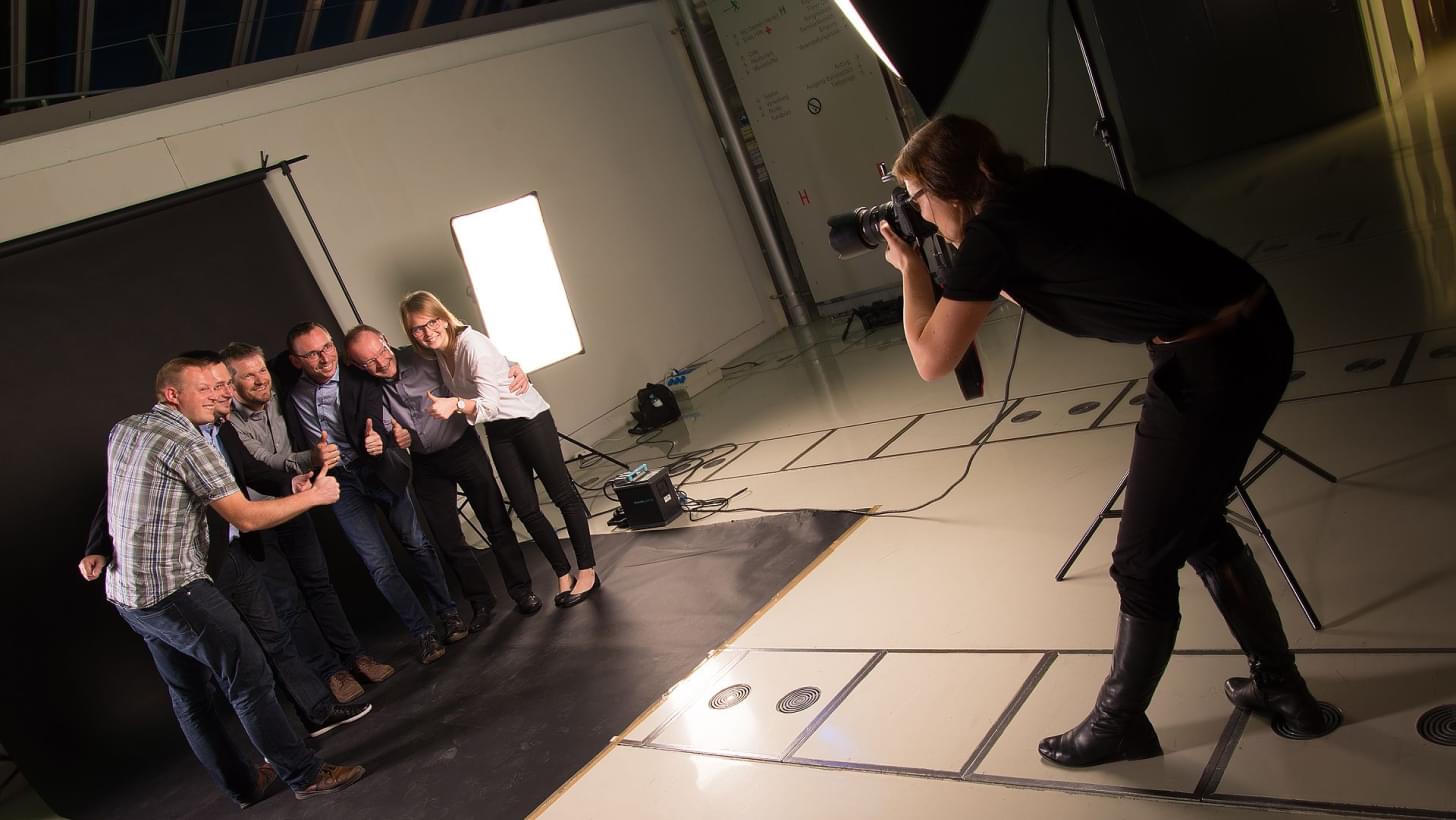 Ein Fotostudio mit mehreren Personen in einer Gruppe, mit einer Fotografin die sie ablichtet.