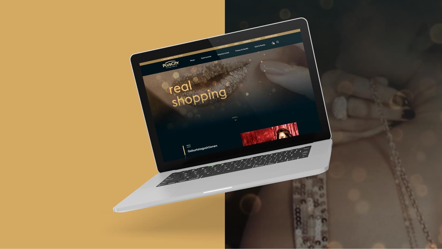 A laptop displays the PLUSCITY website with the phrase “real shopping” on a gold-black background.