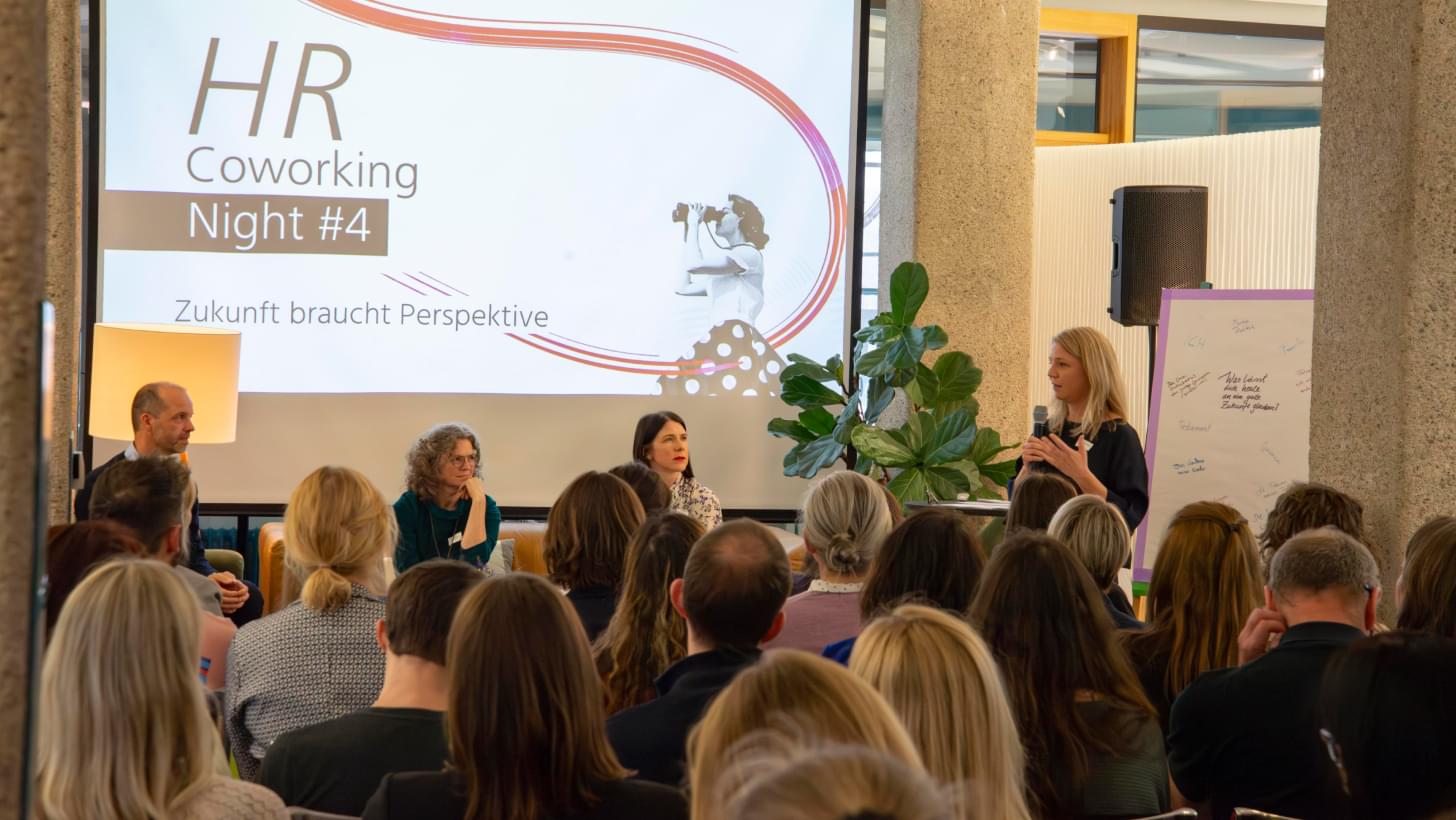 Blick auf das Publikum und die Sprecher:innen der HR Coworking Night #4 mit dem Titel "Zukunft braucht Perspektive".
