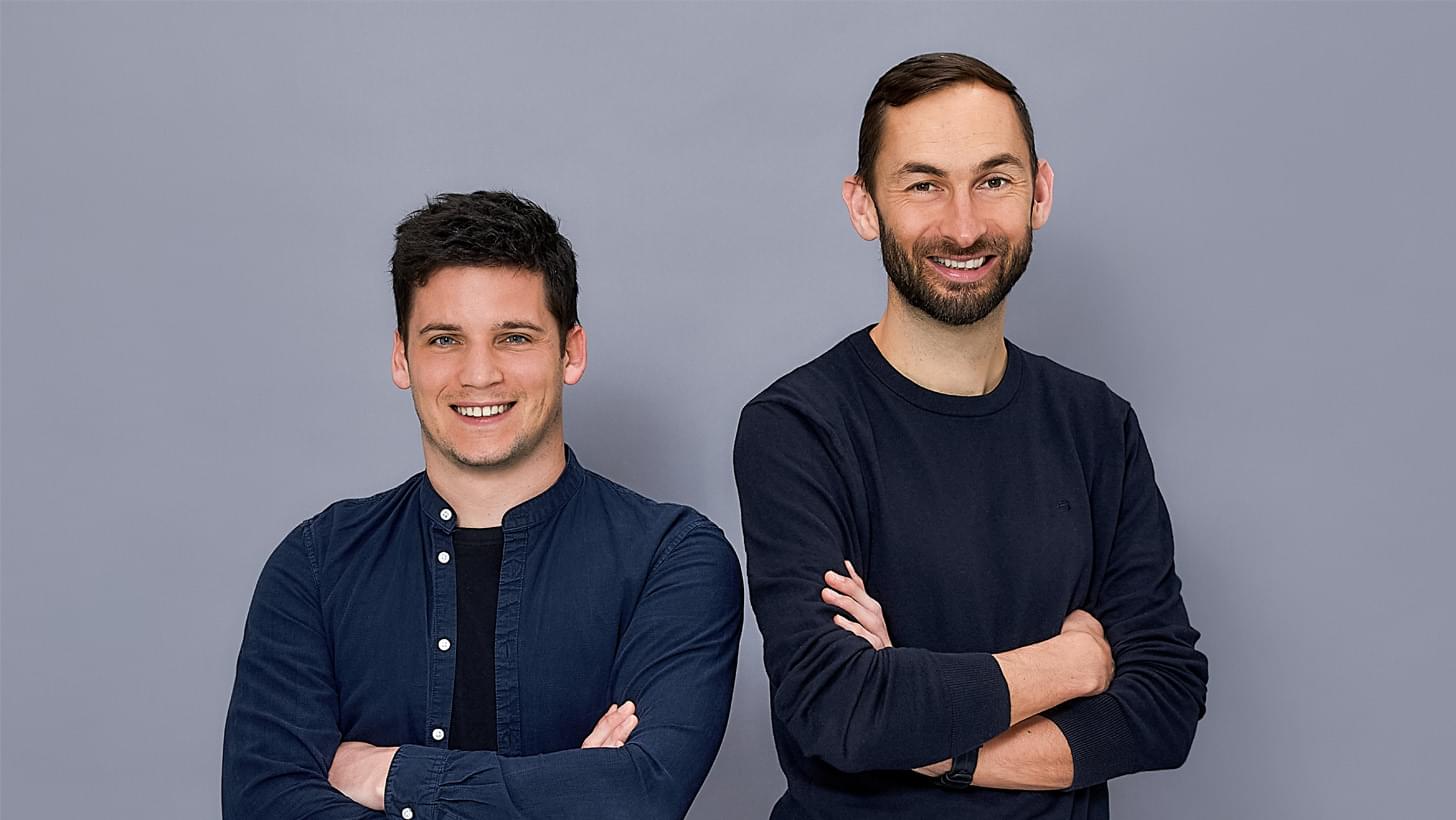 Dominik Strasser and Gernot Bernkopf smiling with arms crossed in front of a grey background.