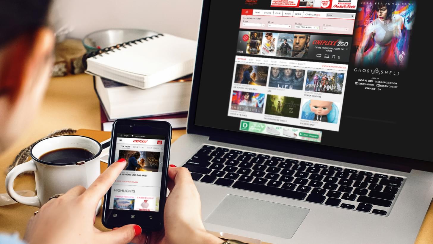 A woman looking at the Cineplexx website on a smartphone and on a laptop.