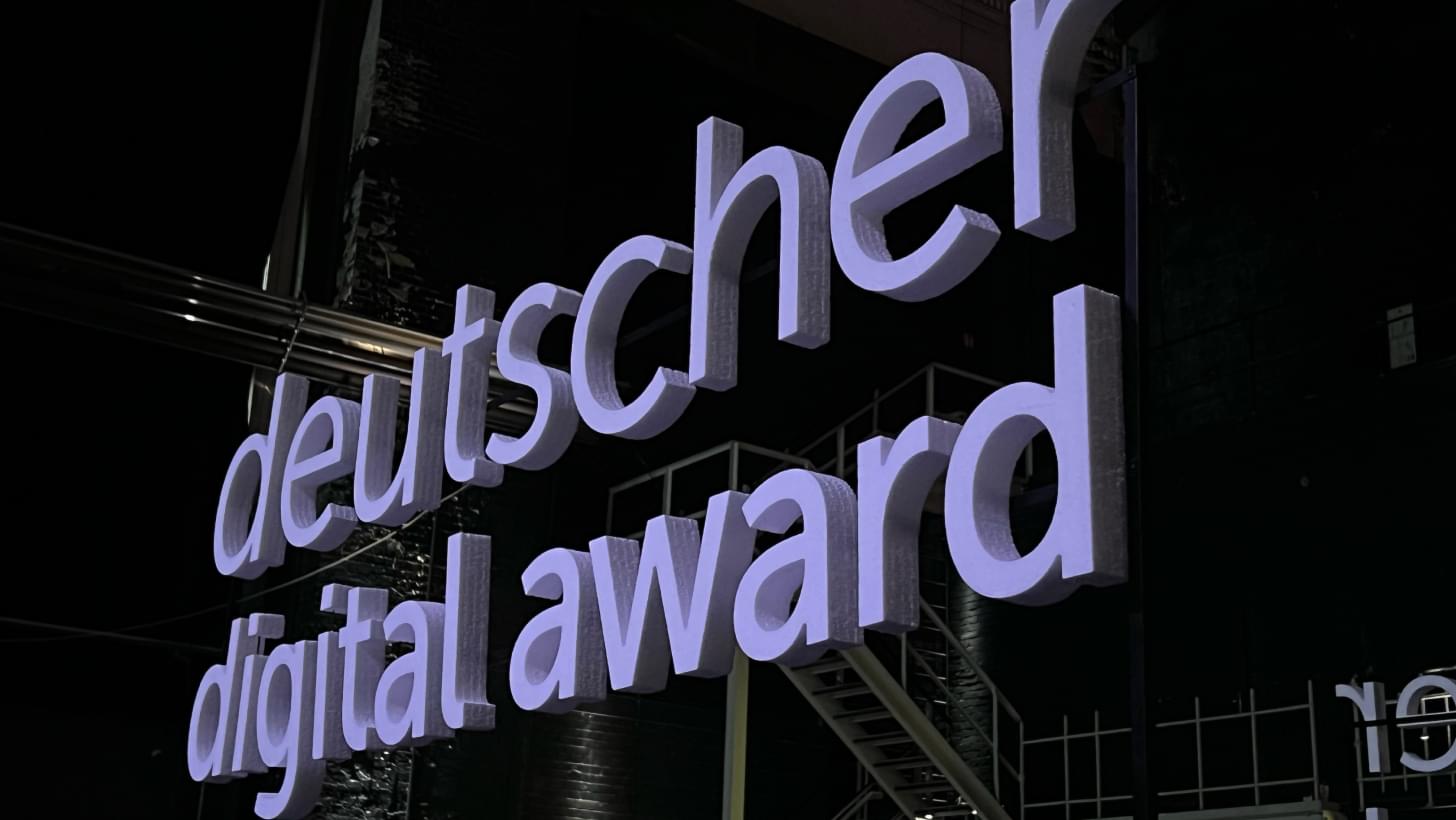 Large illuminated lettering “deutscher digital award” in front of a dark backdrop with industrial architecture.