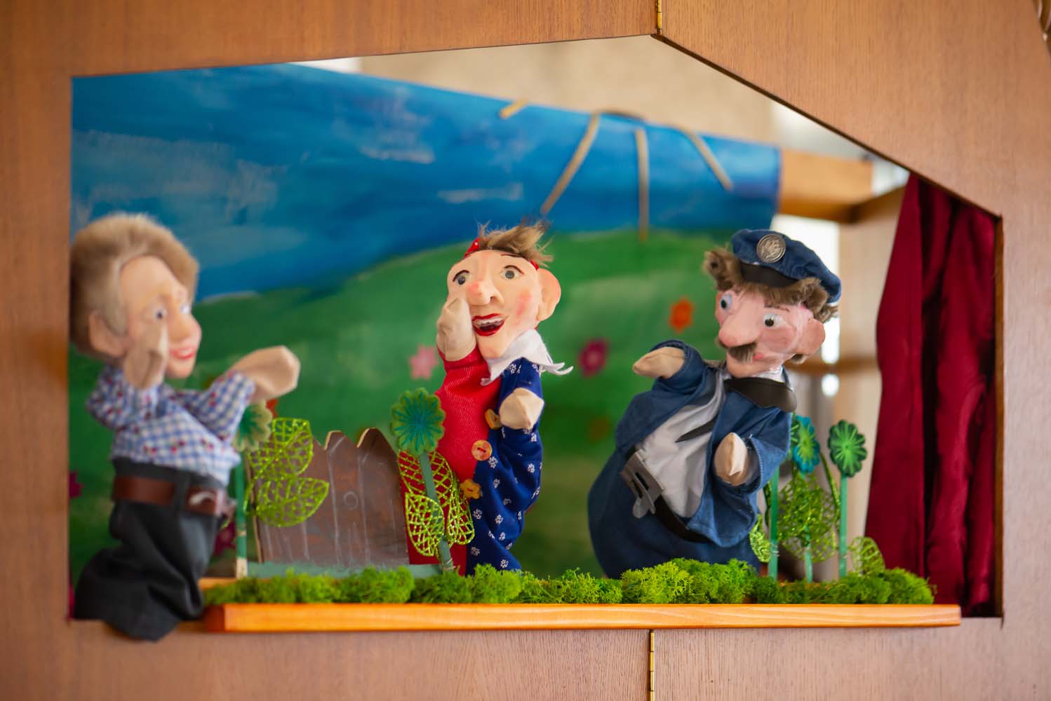 Drei Handpuppen auf einer bunten Puppenbühne, dargestellt vor einer Landschaftskulisse.