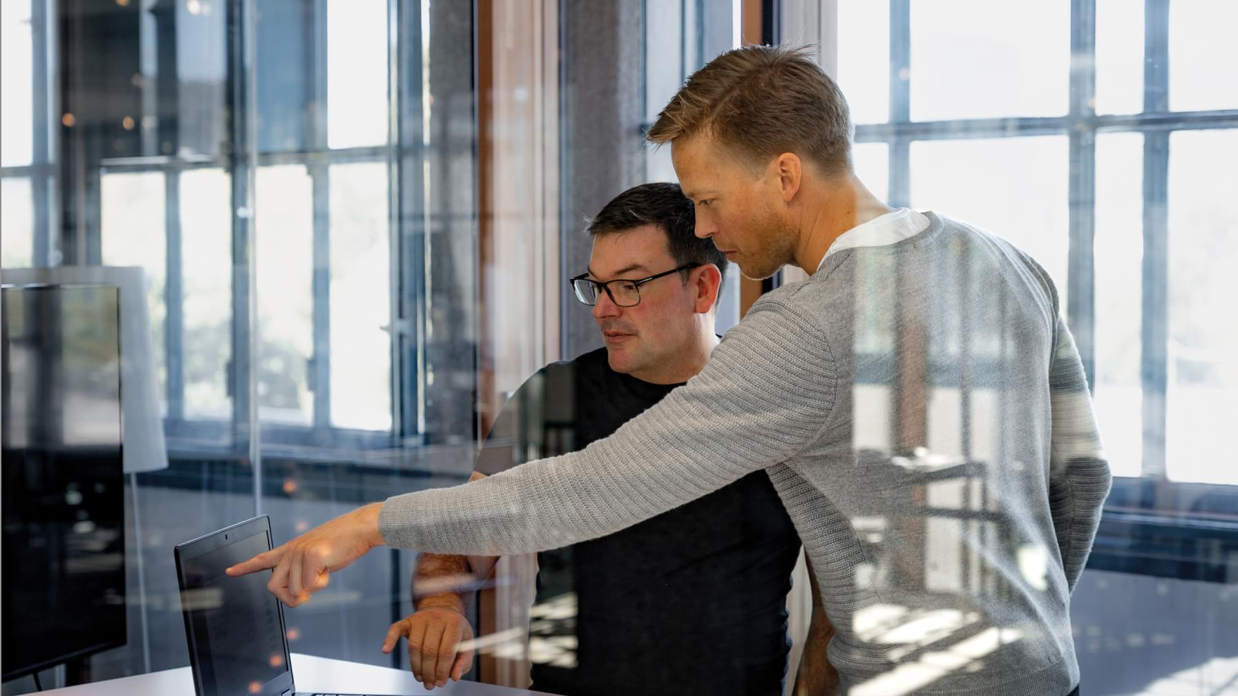 Zwei Männer diskutieren Daten auf einem Bildschirm in einem modernen Büro