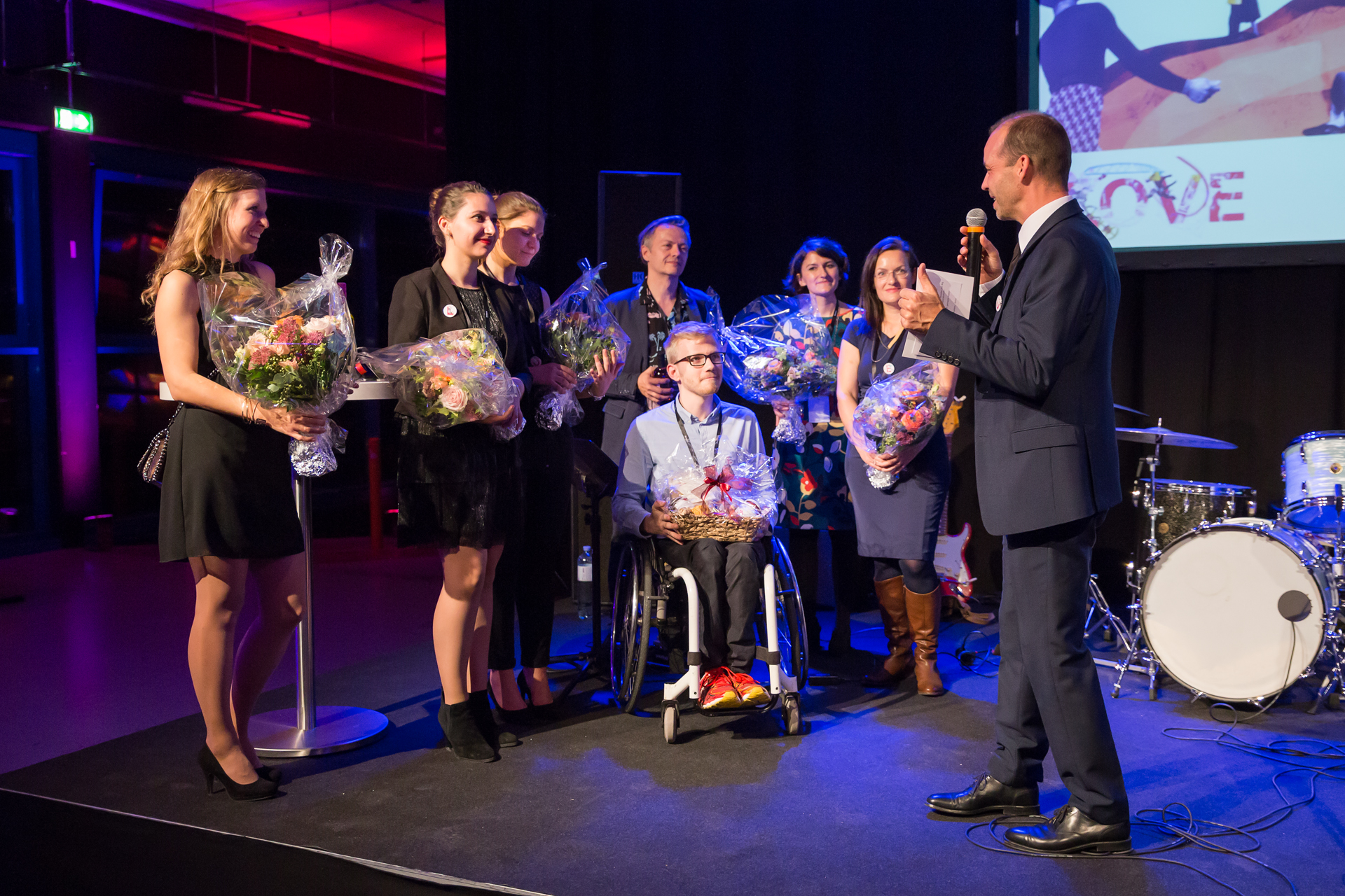 Albert Ortig hands bouquets of flowers to a team on stage, a person in a wheelchair in the middle.