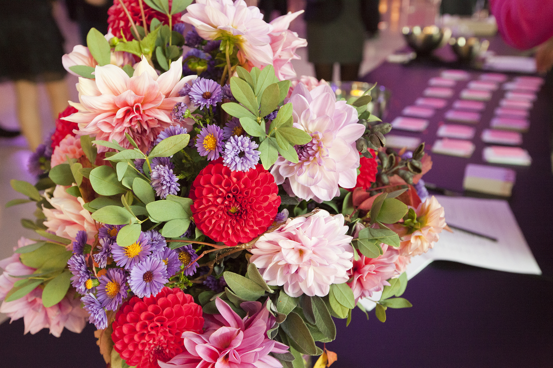 Colorful flower arrangement with red, purple, and pink blossoms on a set table.