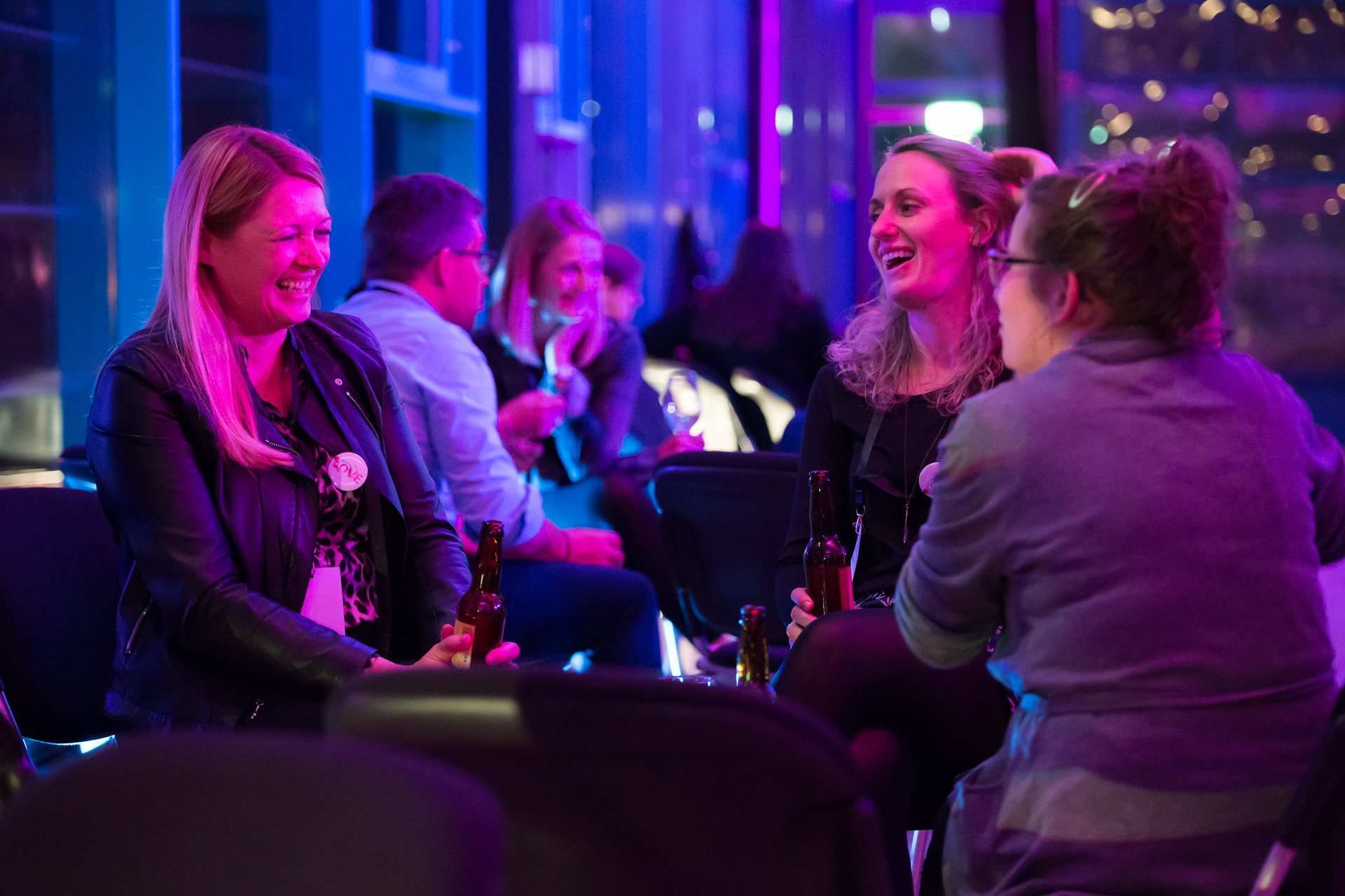 Several women sit relaxed together and chat at an evening event.