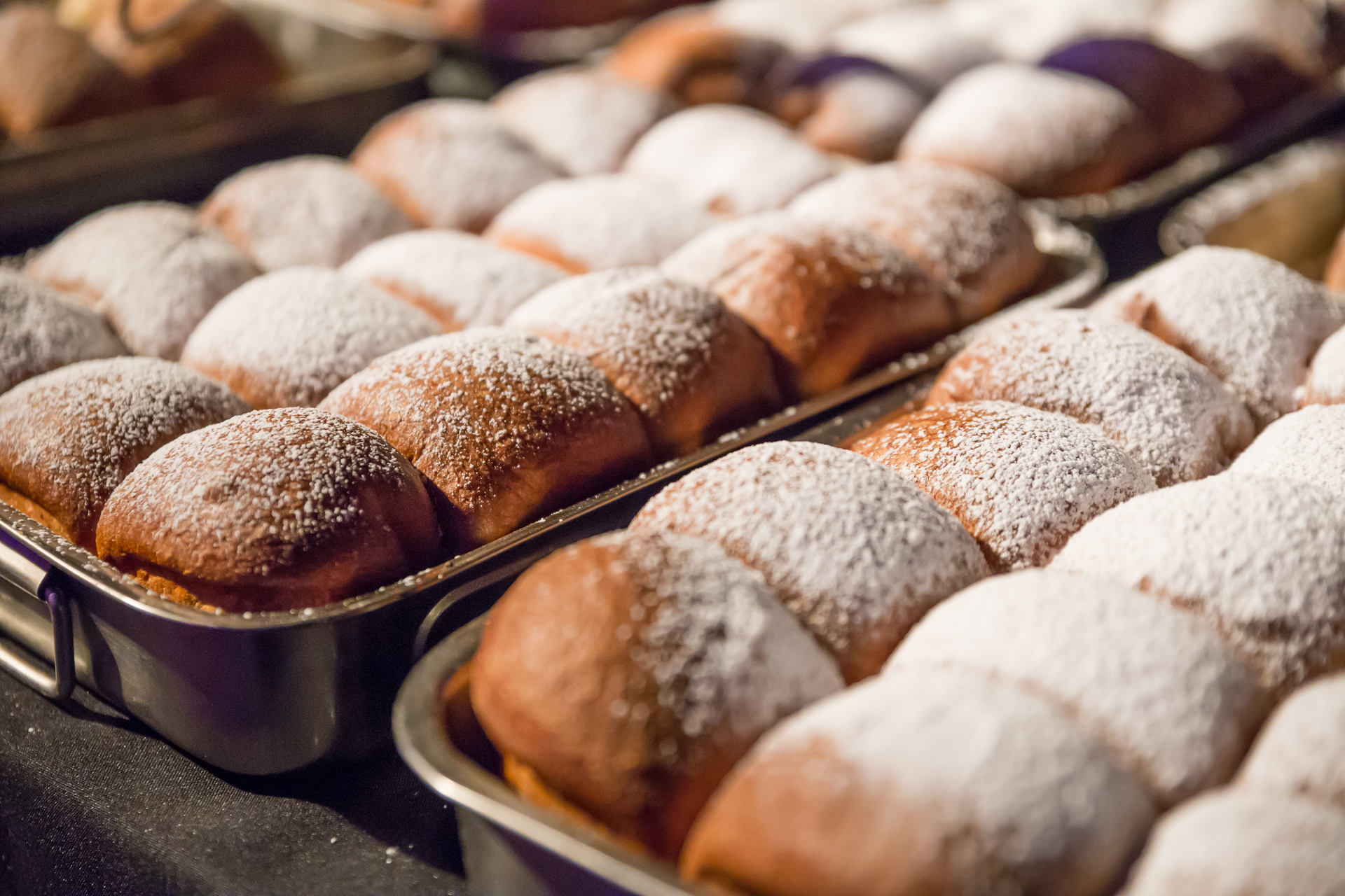 Several baking trays with freshly baked Buchteln (sweet rolls), dusted with powdered sugar.