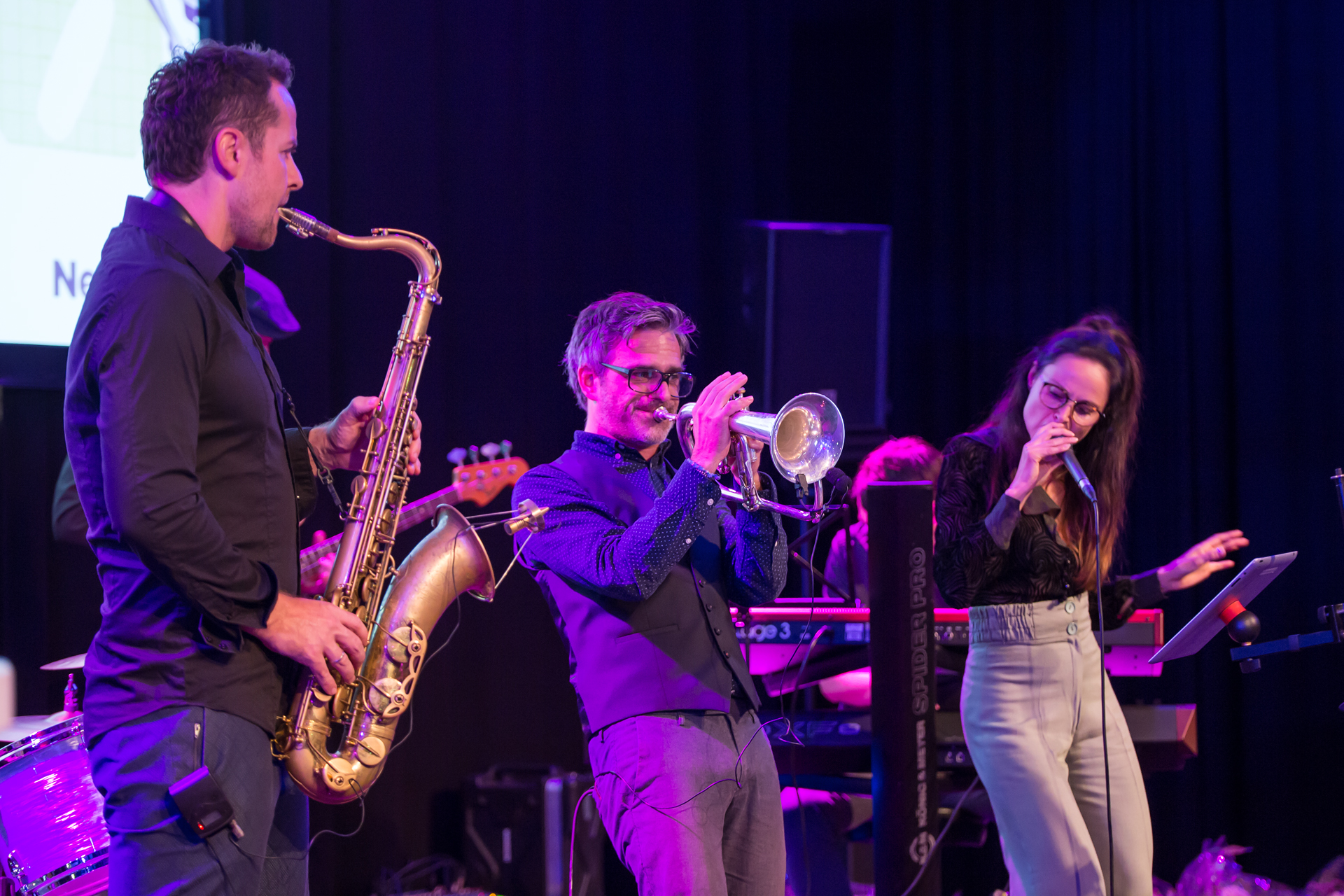 Band plays on stage, musicians on saxophone and trumpet, singer next to them.