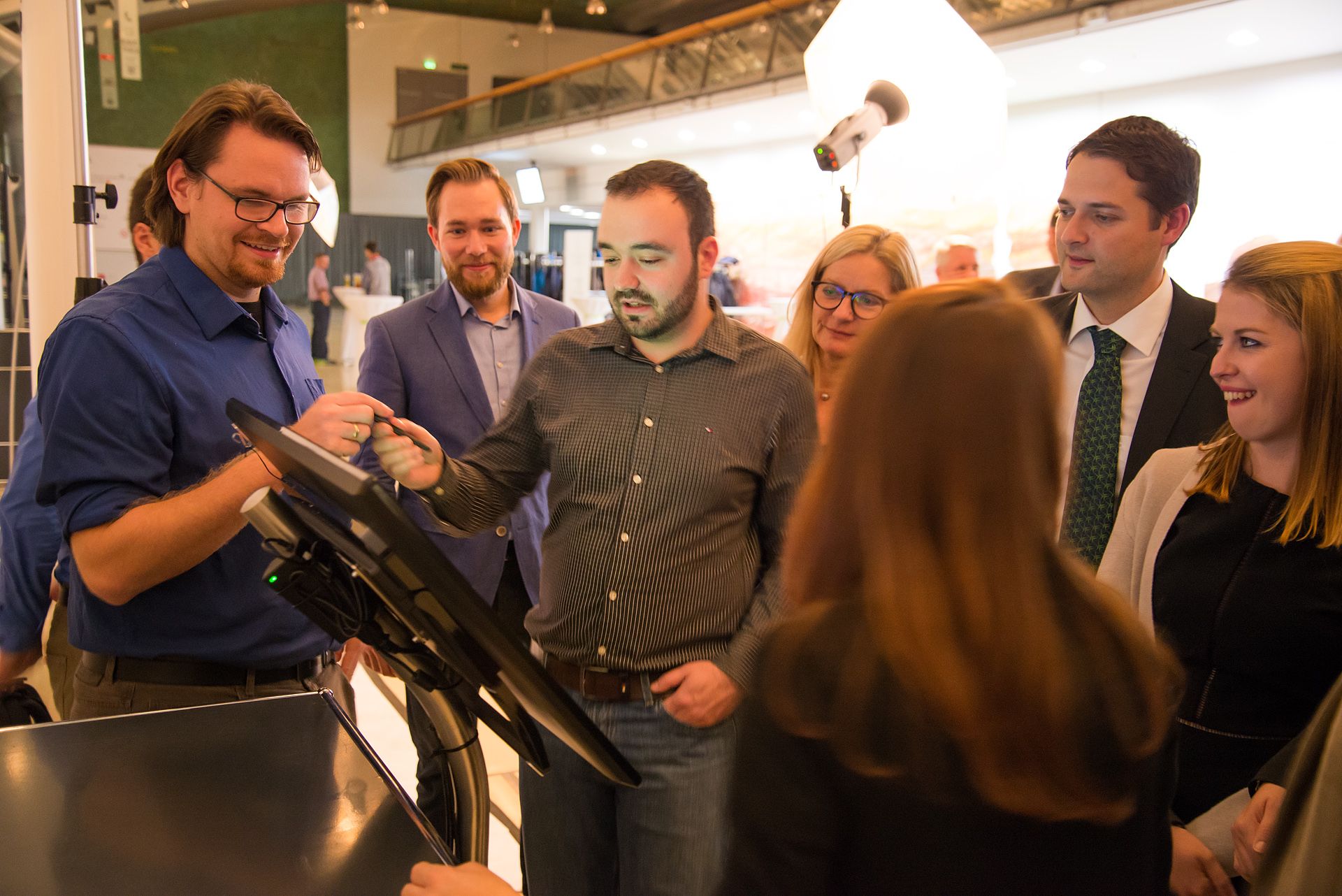 Mehrere Personen stehen um das Touch Terminal, ein Mann reicht einem anderen einen Stylus.
