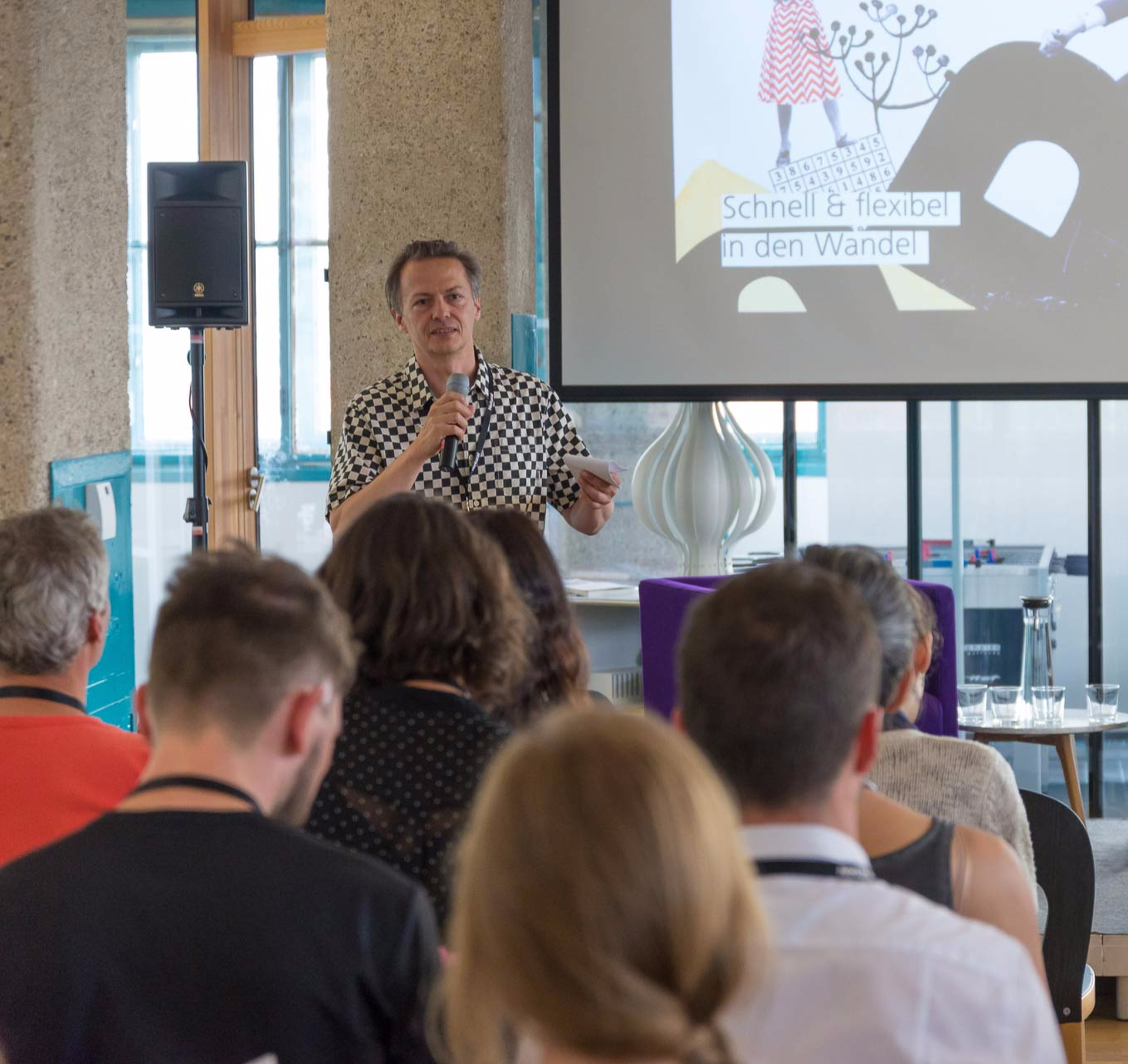 Ernst Demmel (Netural) stands with a microphone in front of an audience and gives a talk on the topic "Fast and Flexible in Times of Change."