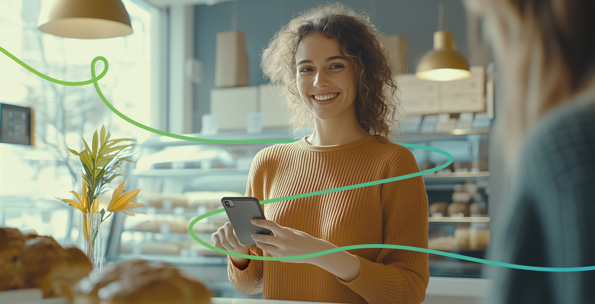 Junge Frau in Bäckerei lächelt und hält ein Smartphone in der Hand, grüne Linie symbolisiert digitale Verbindung.