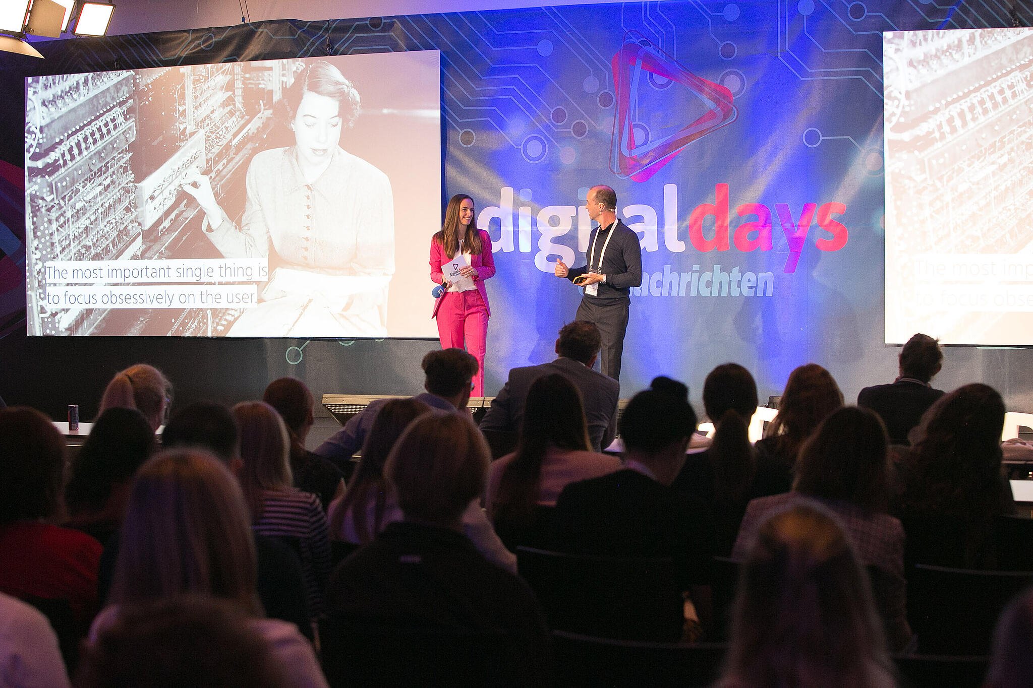 Host and Albert Ortig on stage at Digital Days, audience in the foreground, presentation screen in the background.