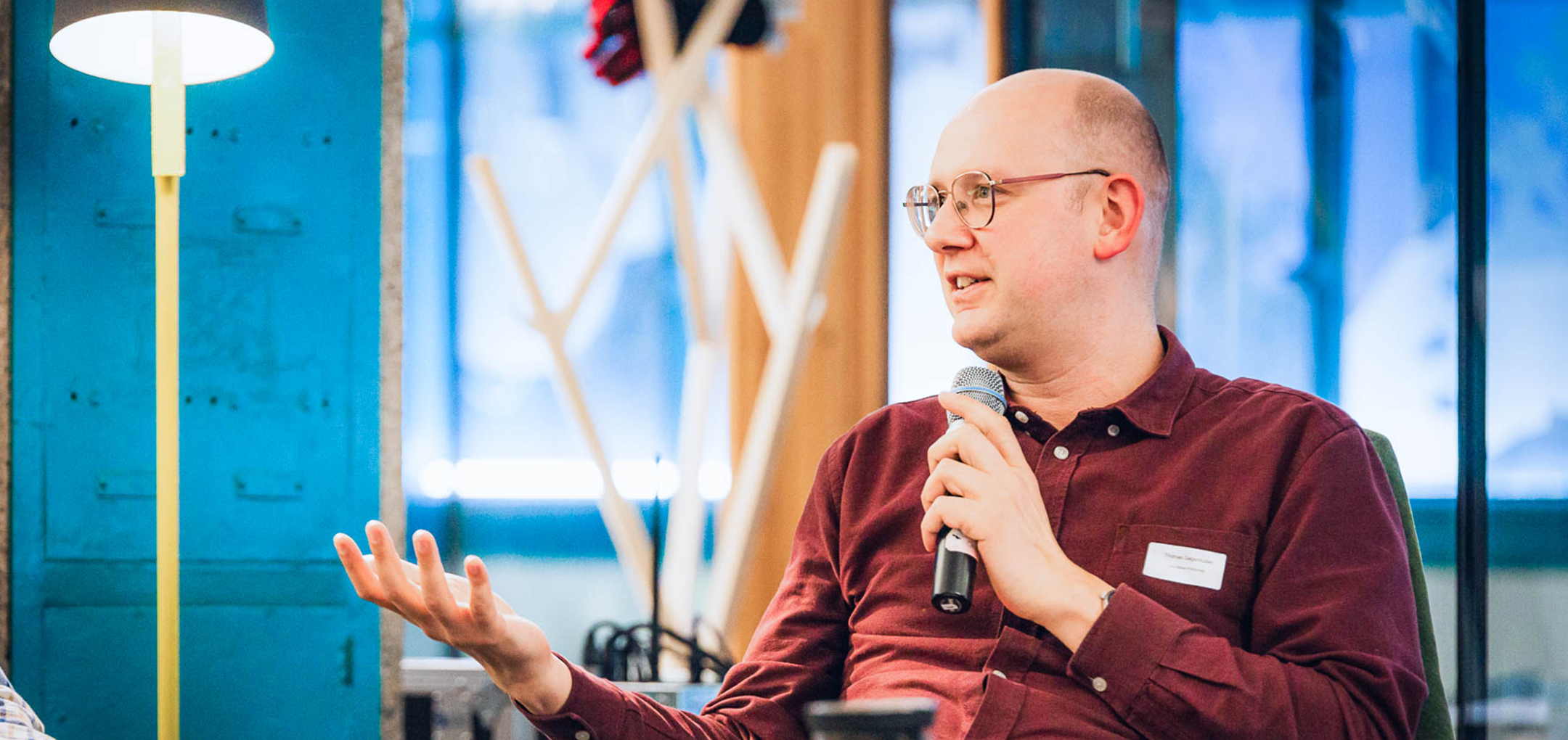 Thomas Gegenhuber spricht während einer Podiumsdiskussion und gestikuliert mit der linken Hand, ein Mikrofon in der rechten.