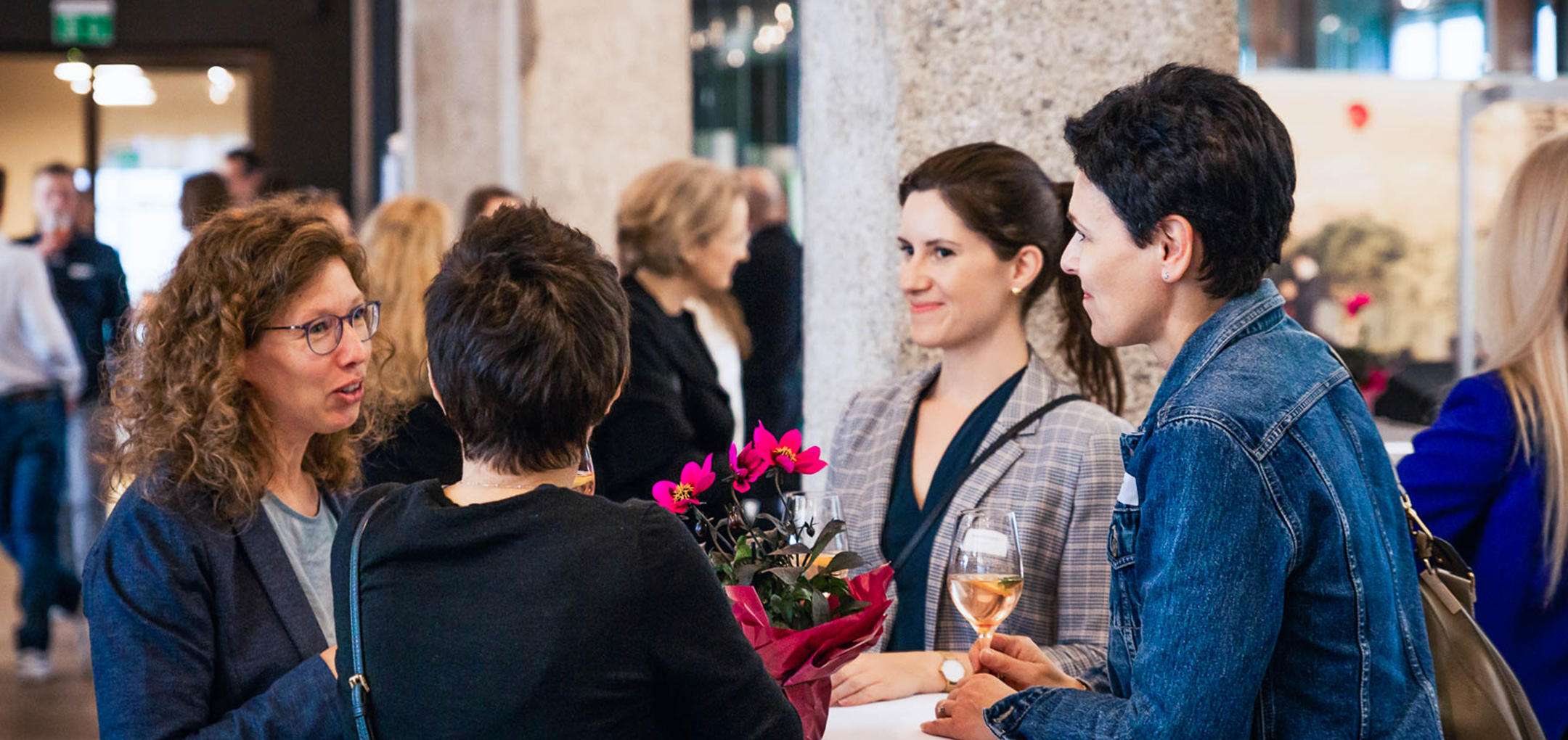 Vier Frauen im Gespräch an einem Stehtisch mit Blumen und Getränken – lebendiger Austausch beim Networking.