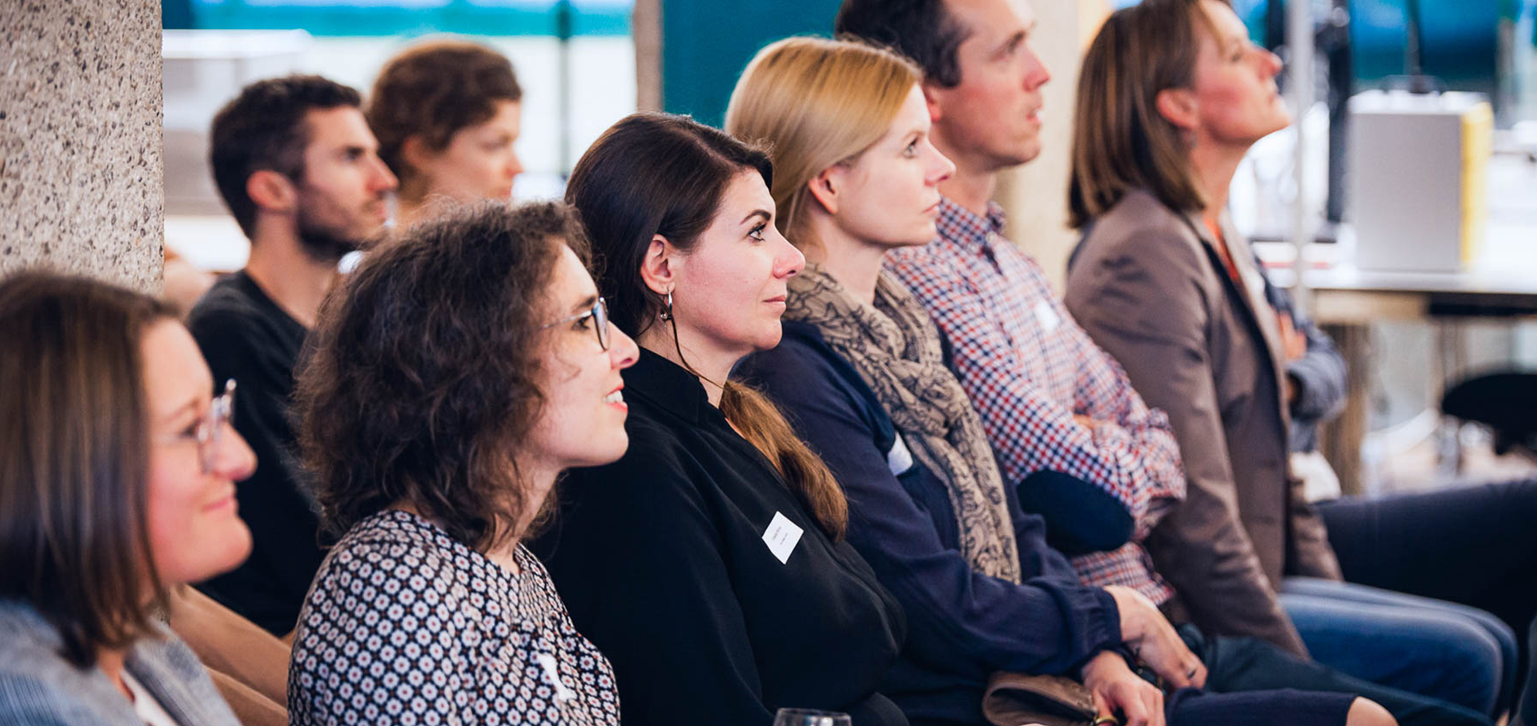 Mehrere Zuhörer:innen in der ersten Reihe verfolgen aufmerksam eine Präsentation oder Diskussion zum Thema KI.
