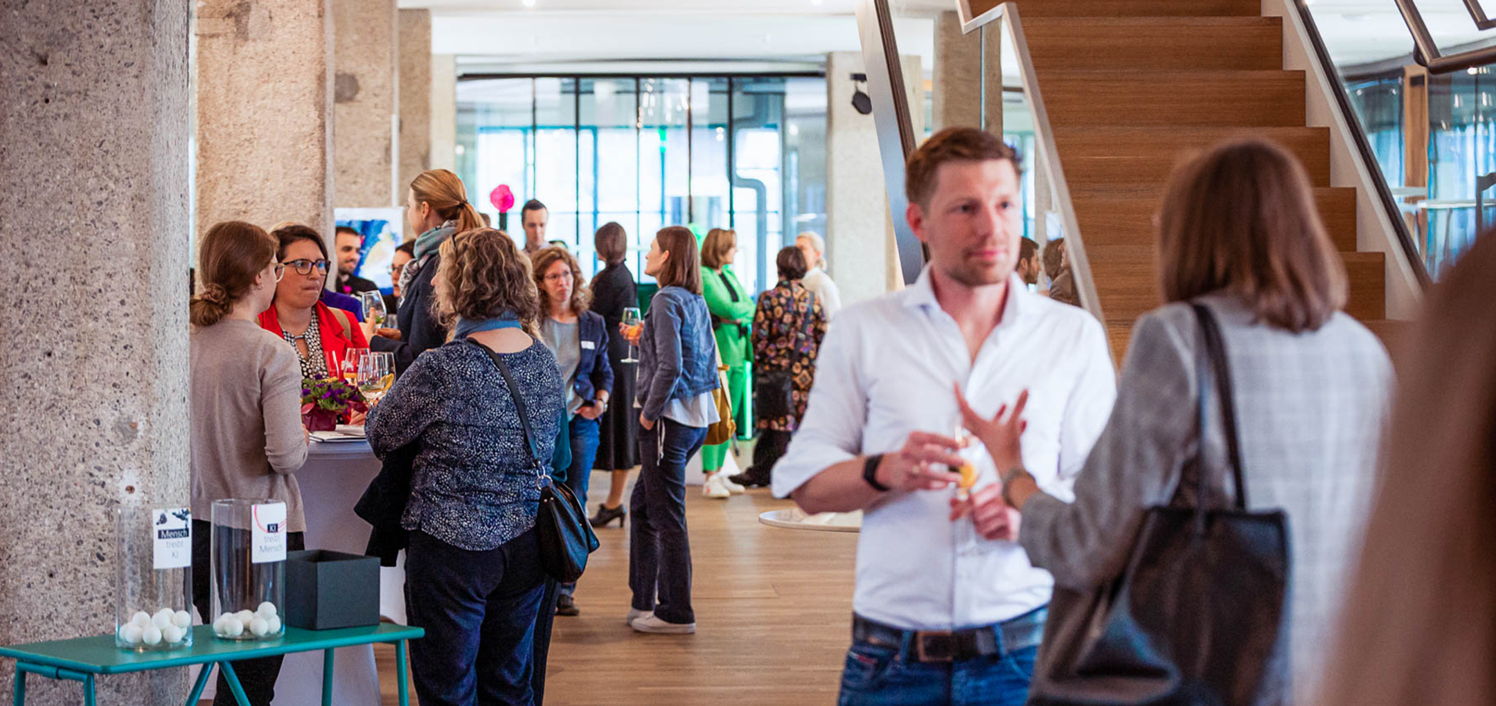 Menschen im lebendigen Austausch in einem offenen Foyerbereich – informelles Networking bei der Veranstaltung „Mensch & KI“.