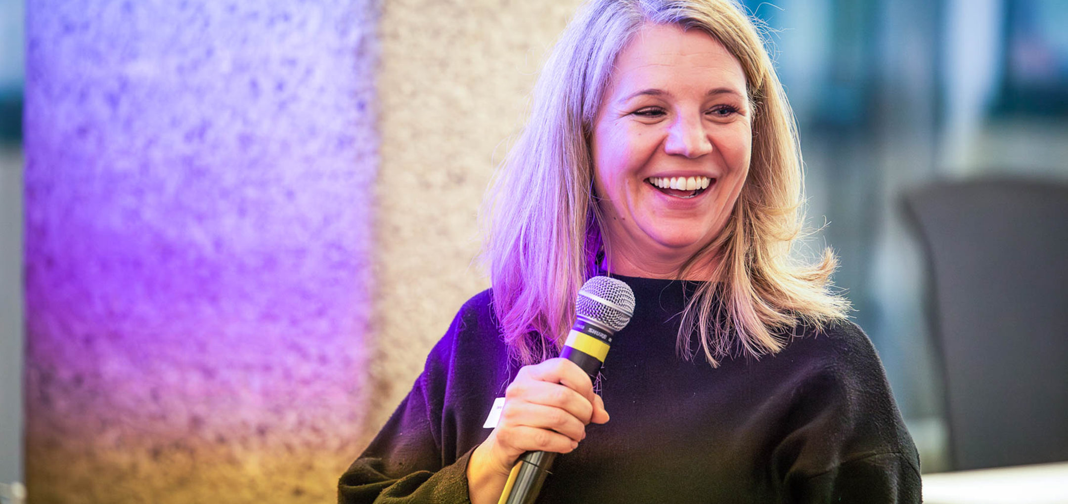 Irene Bouchal-Gahleitner lächelt herzlich und hält ein Mikrofon – sie moderiert einen Programmpunkt der Veranstaltung.