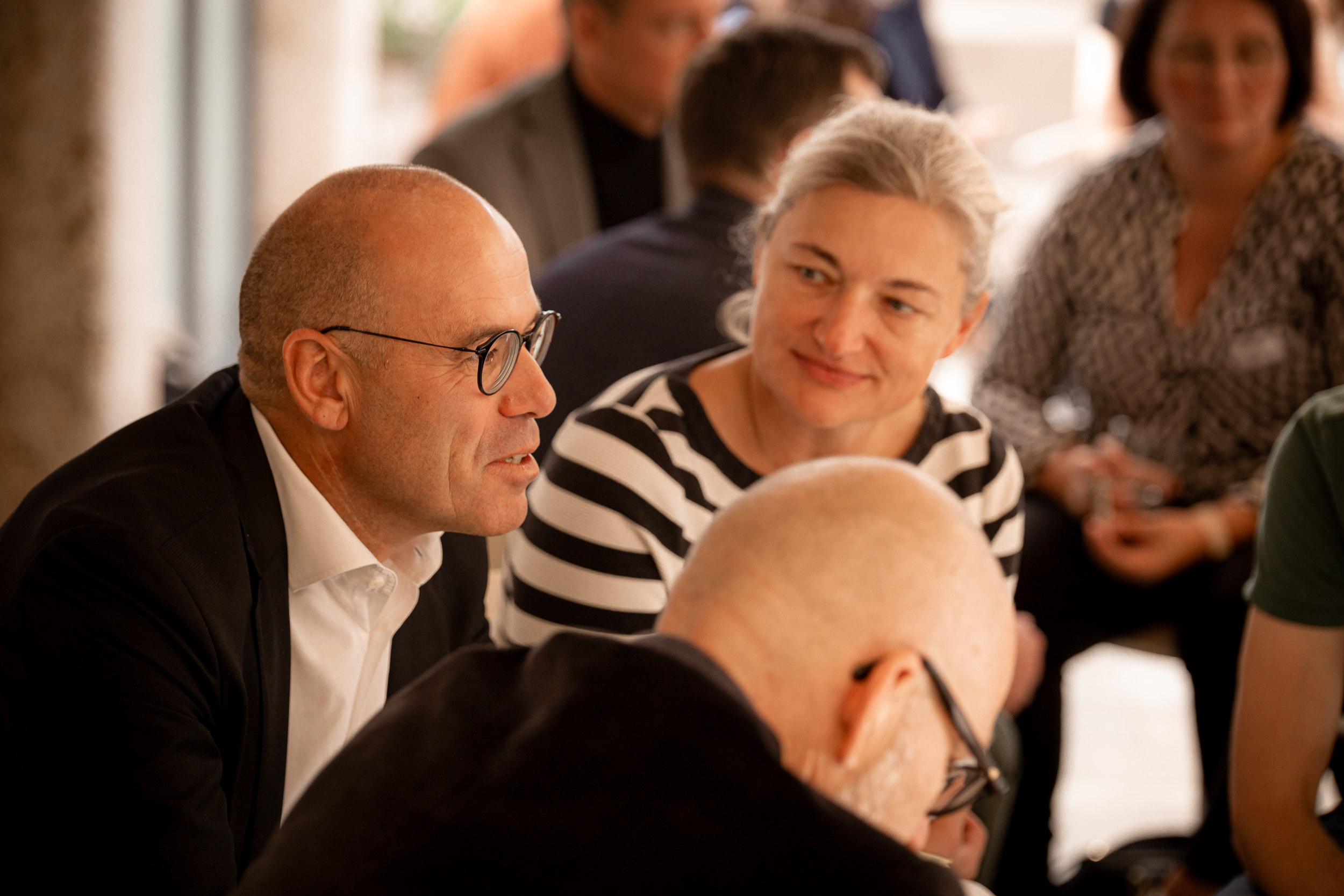 People in conversation at Netural’s AI Impulse Breakfast – in focus are a man in a suit and a woman in a striped shirt.