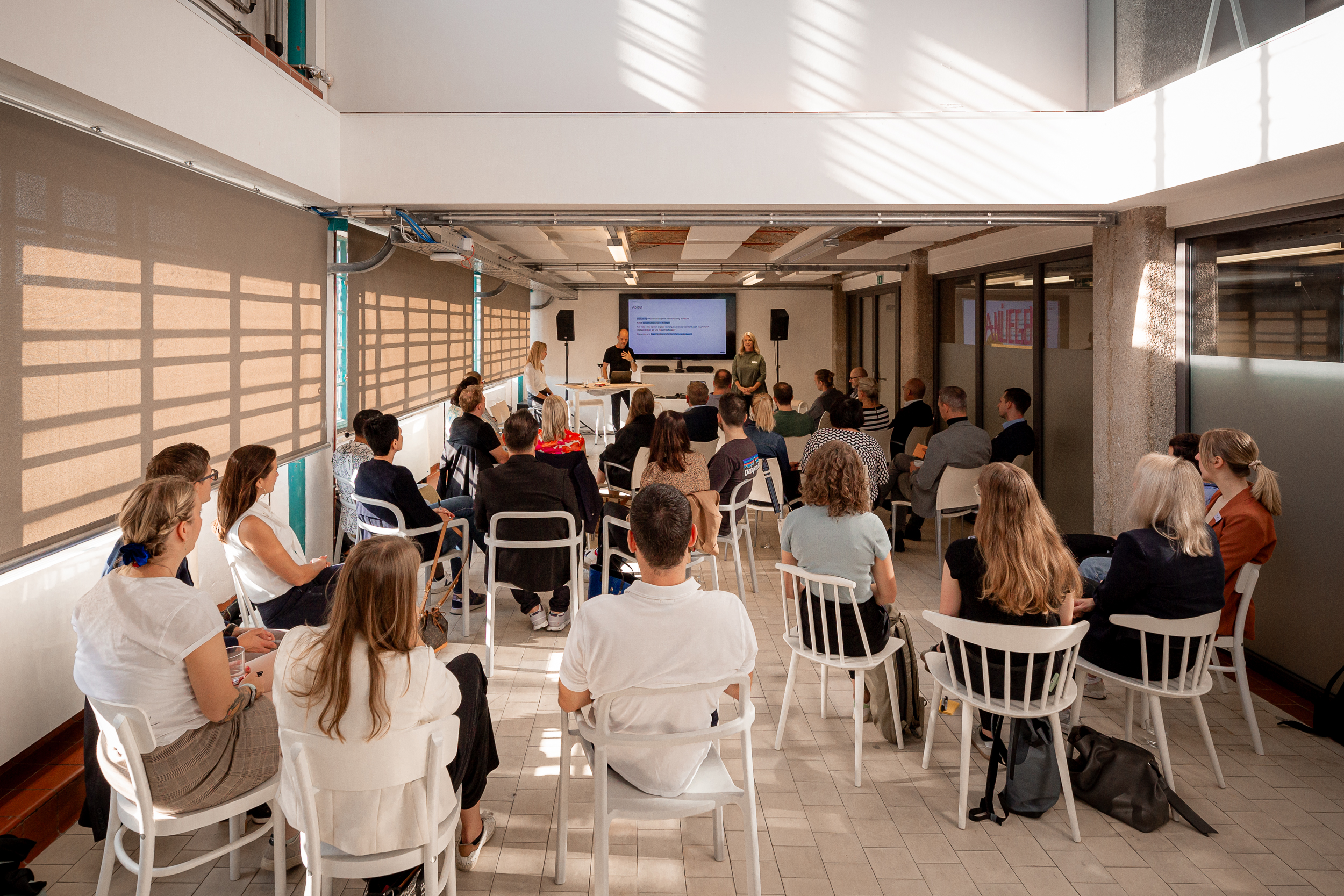 Presentation at Netural’s AI Impulse Breakfast: participants seated in rows, with three speakers at the front in front of a screen.