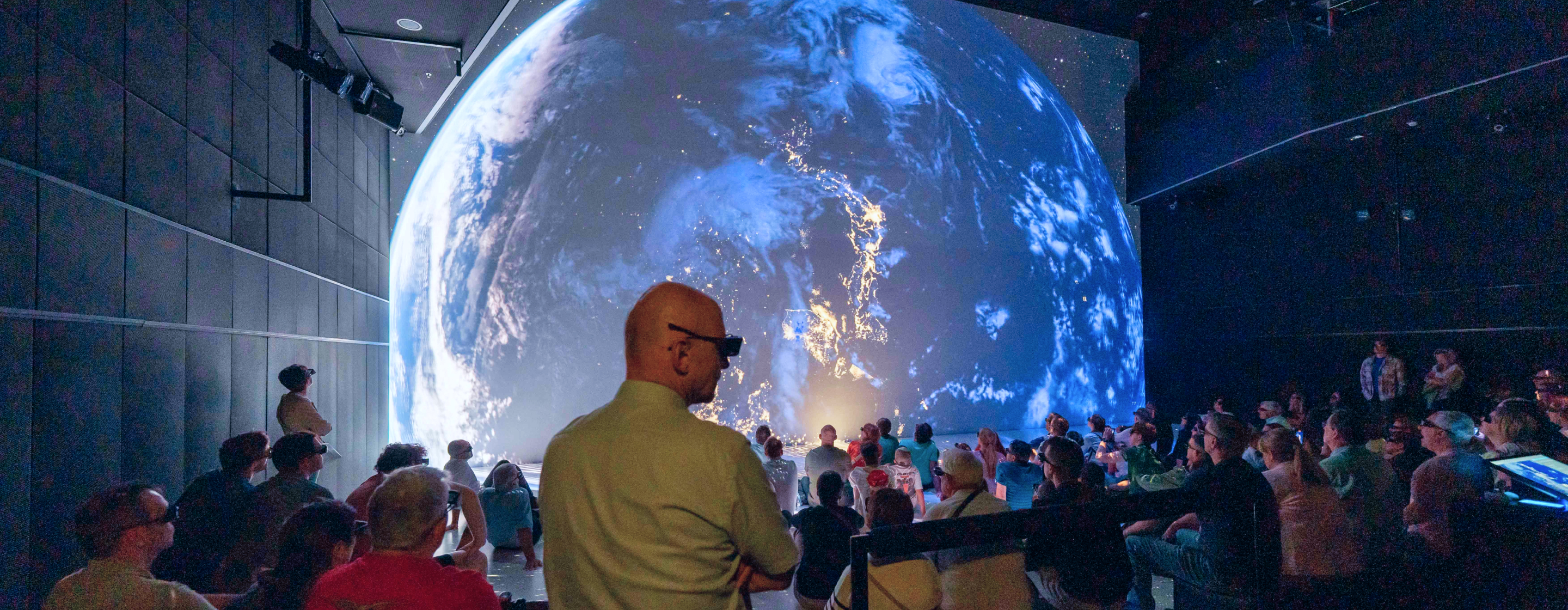 Teilnehmer erleben immersive Projektion eines Globus im dunklen Raum.