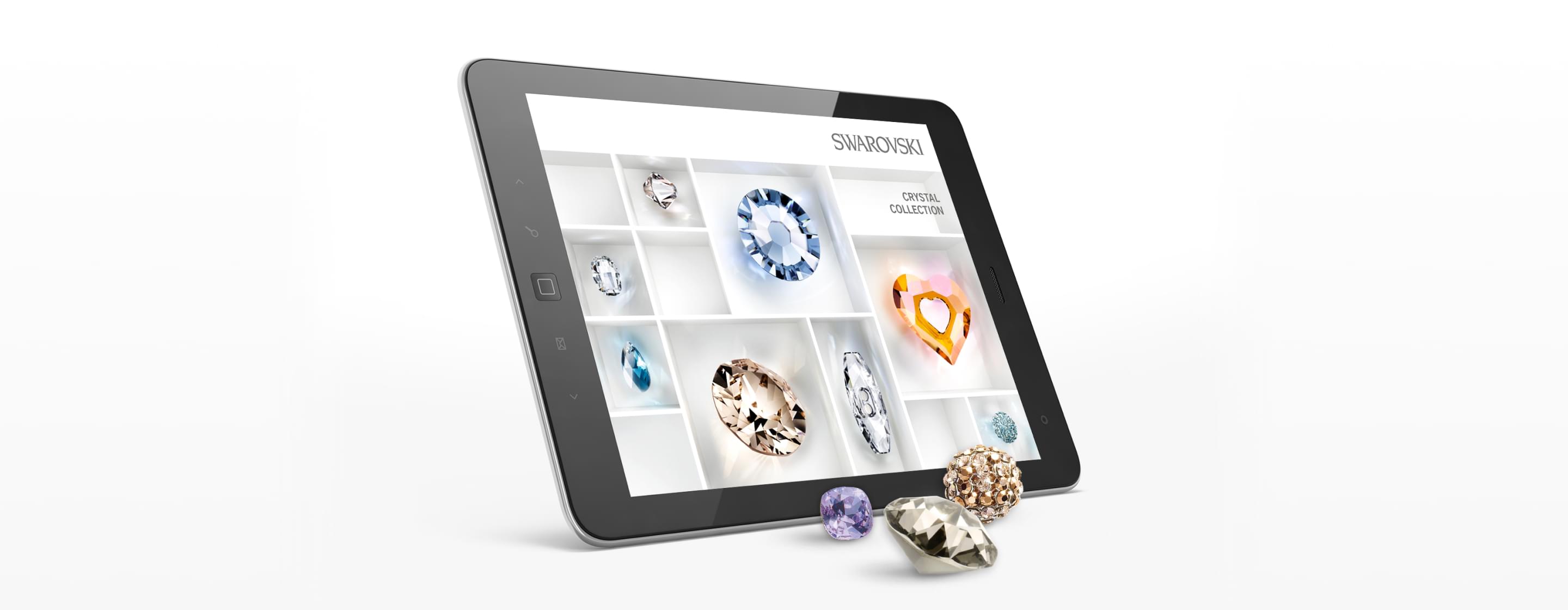 Tablet mit geöffneter Swarovski Crystal Collection App, zeigt Kristalle in Fächern; einige Edelsteine liegen davor.