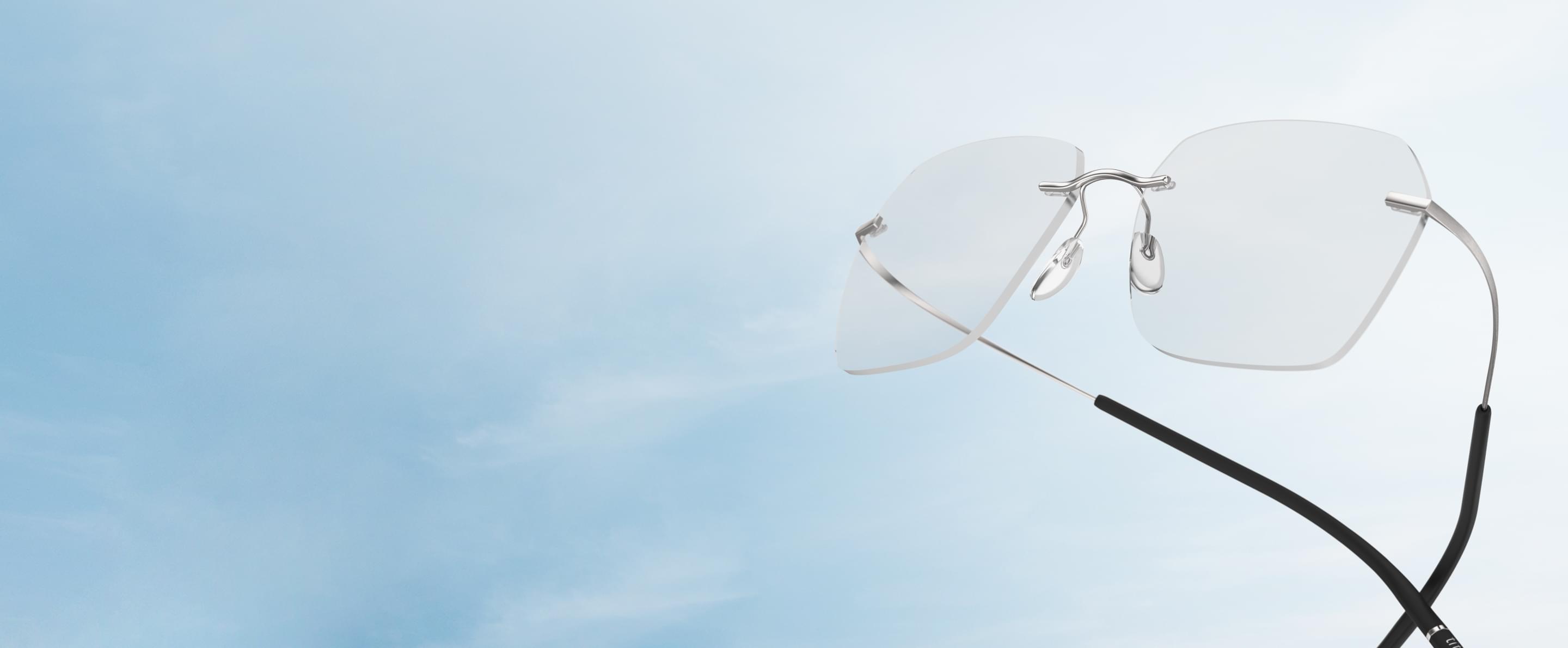 Eine moderne randlose Brille von Silhouette schwebt vor einem hellblauen Himmel.