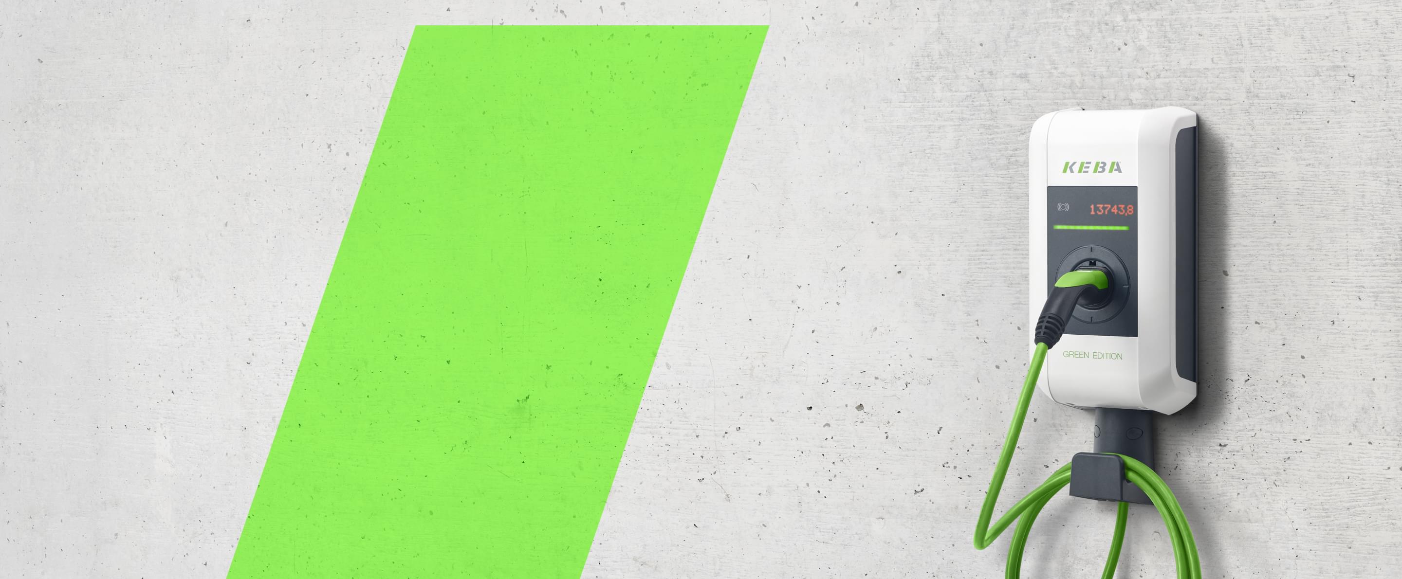 Weiße E-Ladestation mit grünem Ladekabel an einer Betonwand.