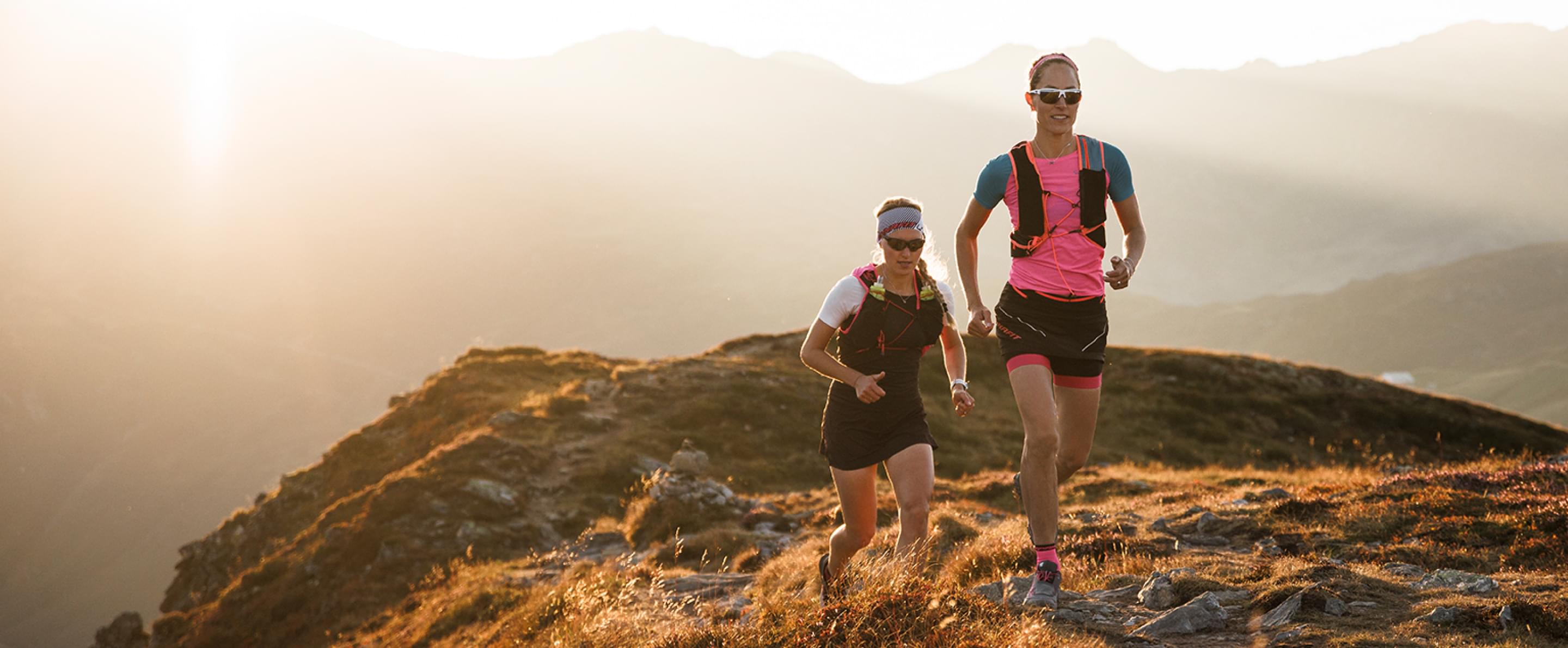 Zwei Frauen mit evil eye Sportbrillen laufen in einer Berglandschaft.