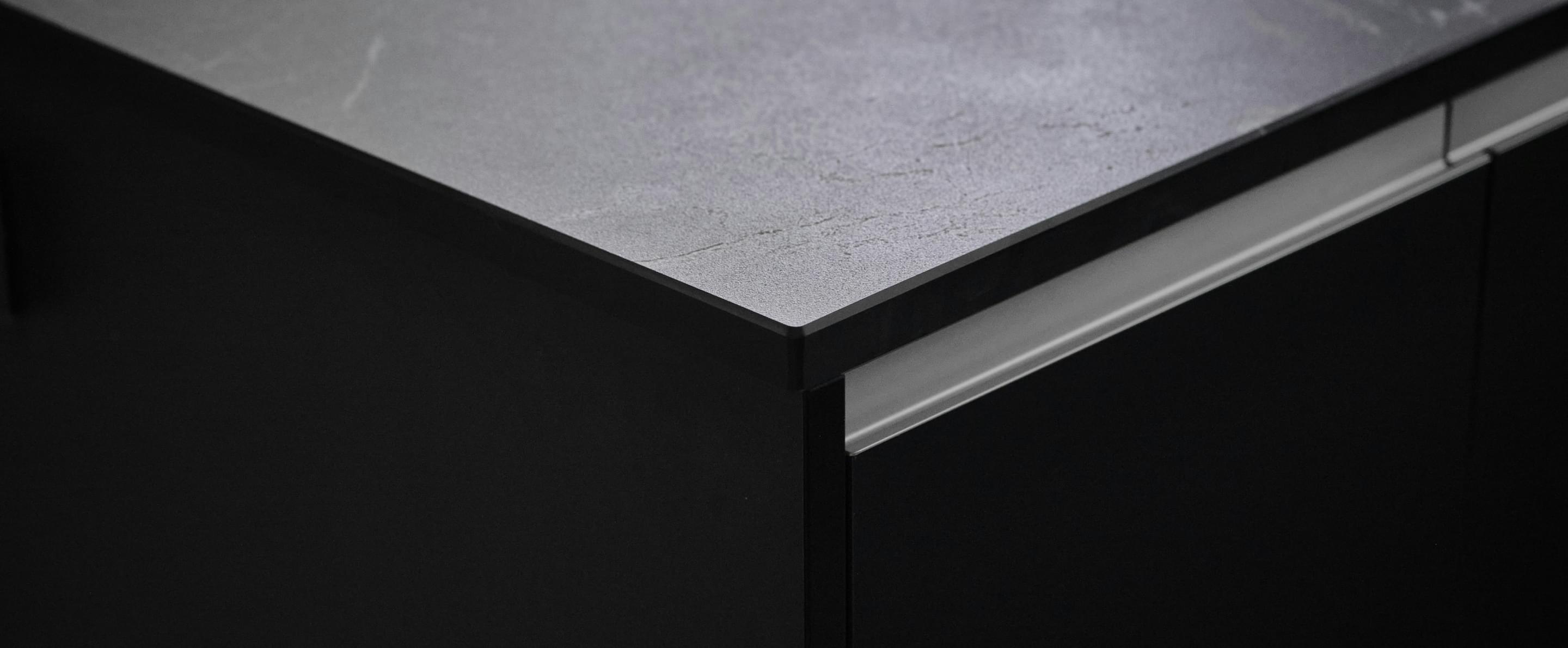 Detailaufnahme einer modernen Küchenarbeitsplatte mit dunkler, matter Oberfläche und klarer Linienführung.