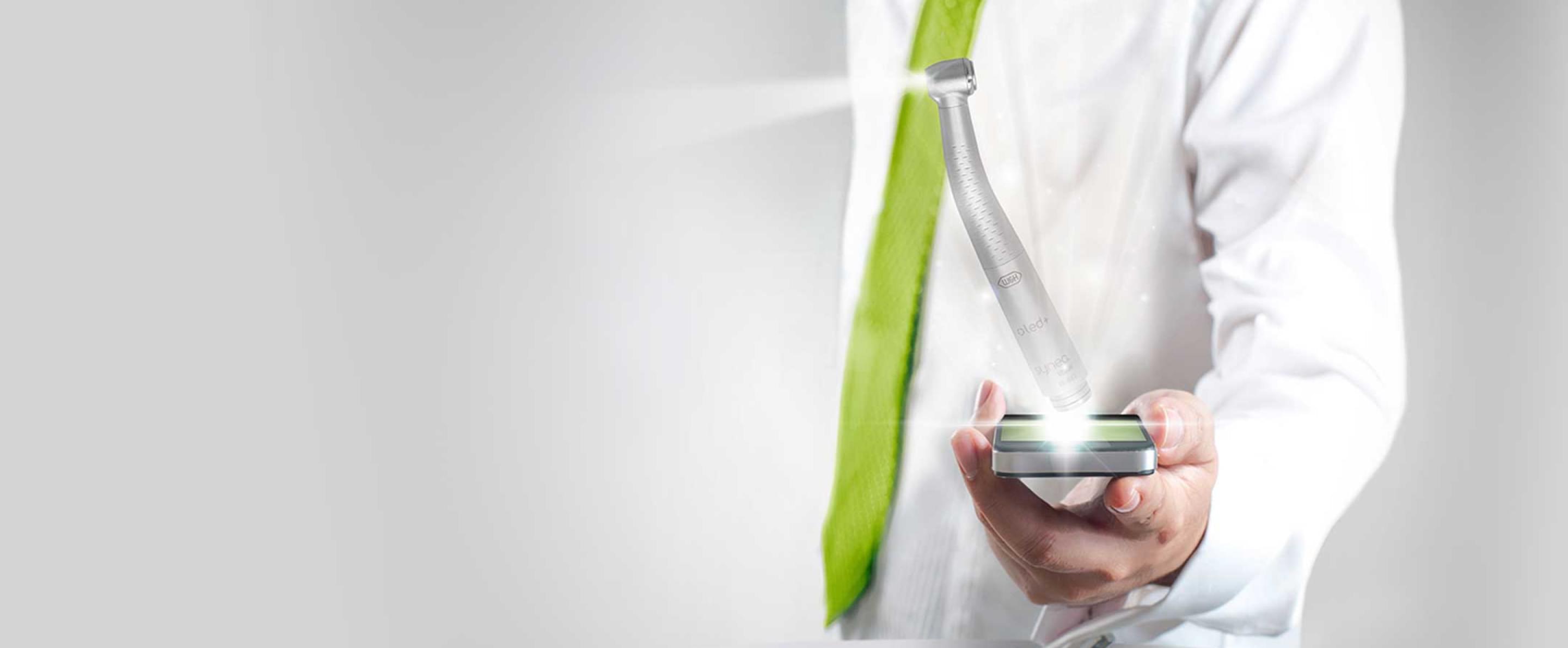 Ein Mann im weißen Laborkittel hält ein beleuchtetes W&H Dentalhandstück – Symbol für Präzision und Innovation.