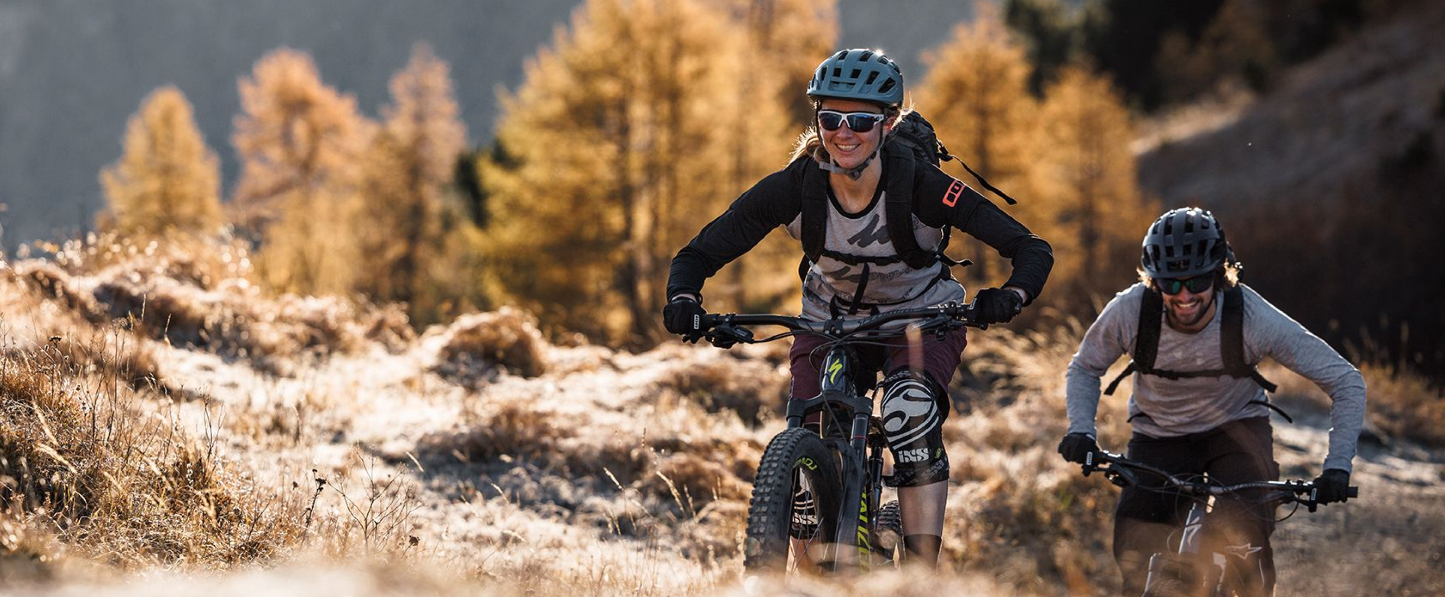 Eine Frau und ein Mann fahren mit Mountainbikes in einer Berglandschaft, sie tragen evil eye Sportbrillen.