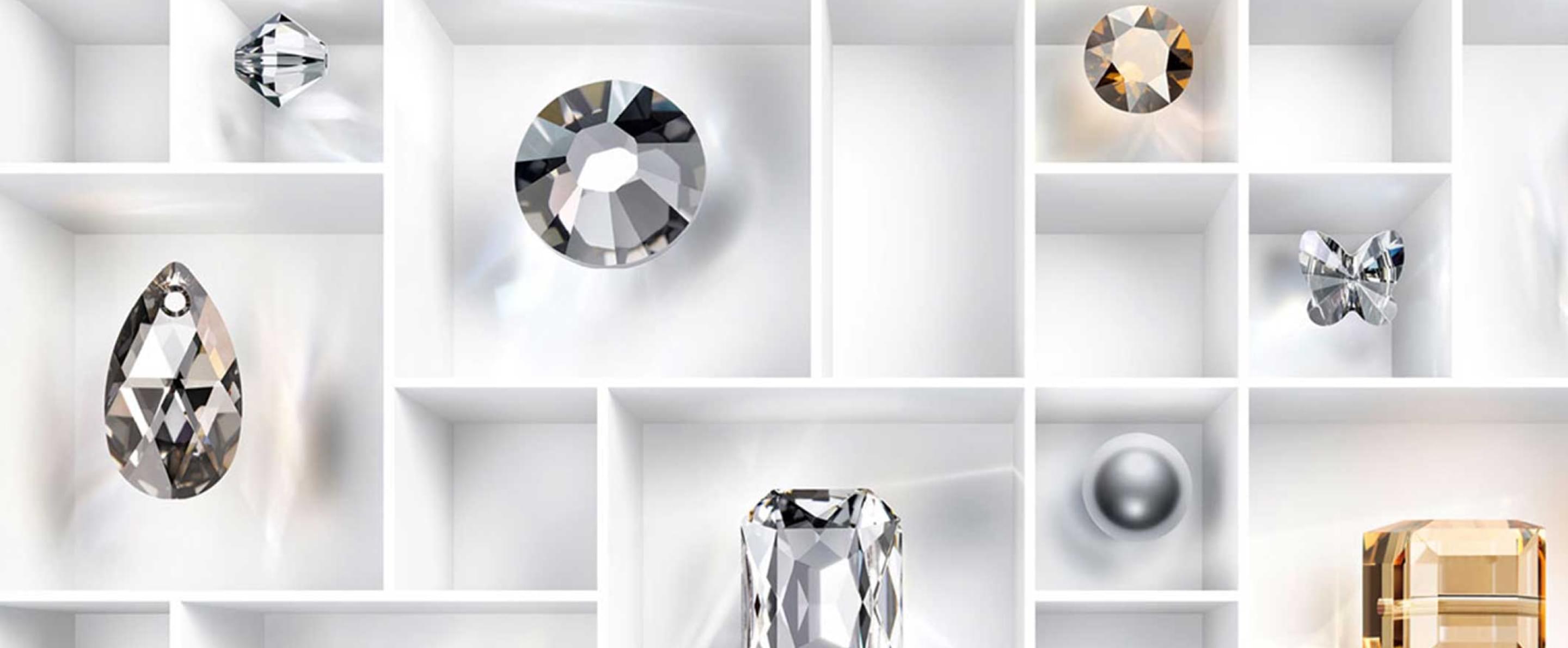 Verschiedene geschliffene Swarovski Kristalle in unterschiedlichen Formen und Farben, arrangiert in einem weißen Fächerkasten.