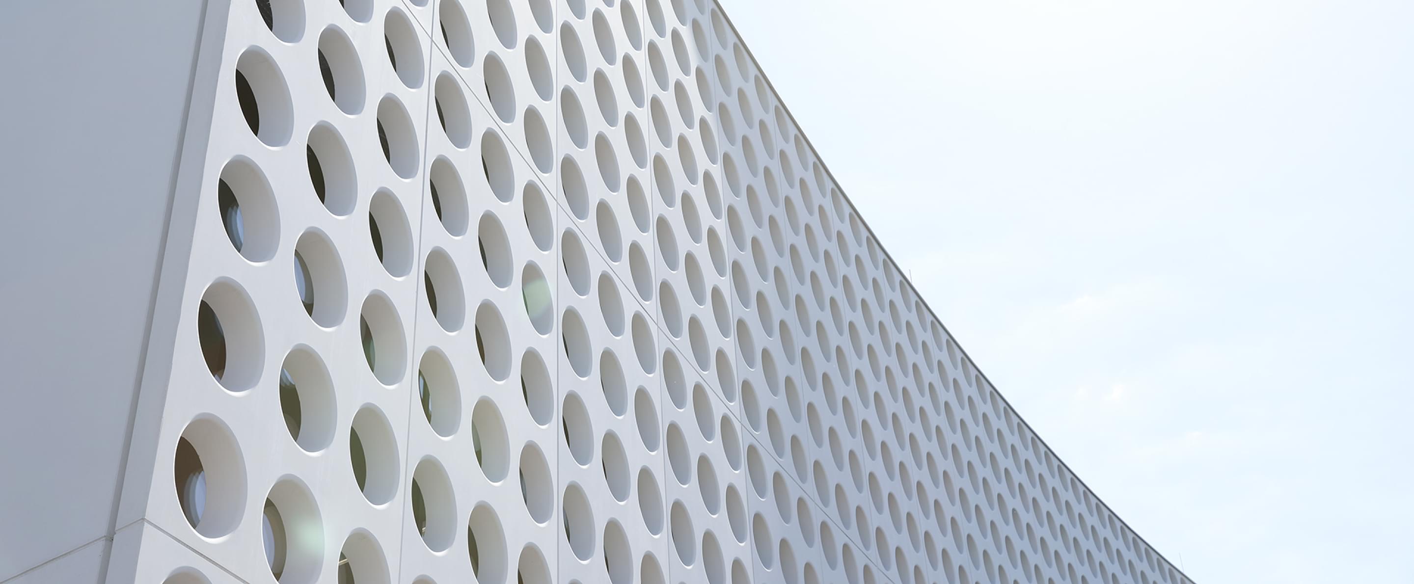 Ansicht der weißen, perforierten Fassade des Silhouette Lens Lab mit runden Öffnungen.