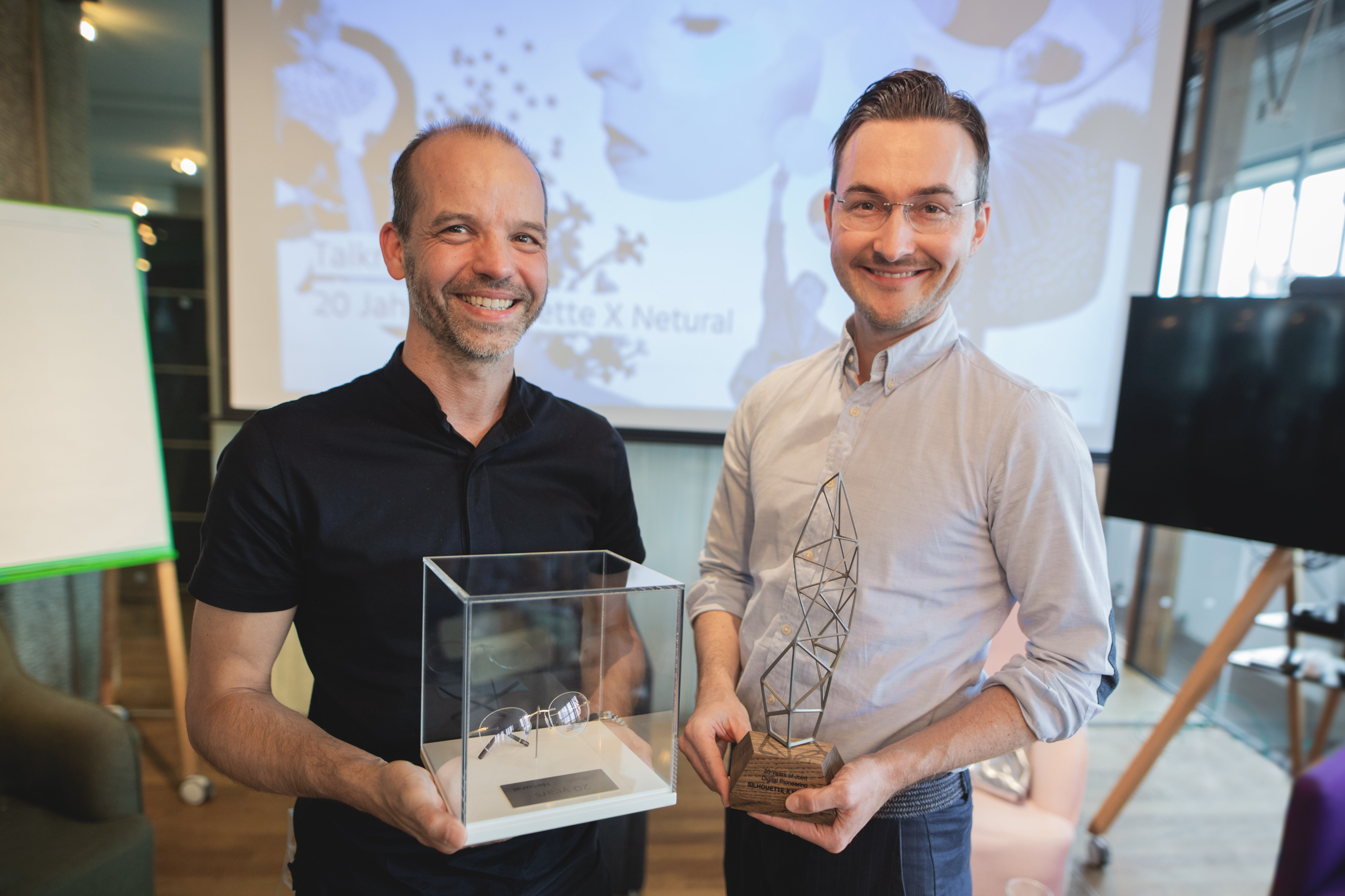 Albert Ortig and Michael Schmied hold awards and smile at the camera at “20 years Netural X Netural”.