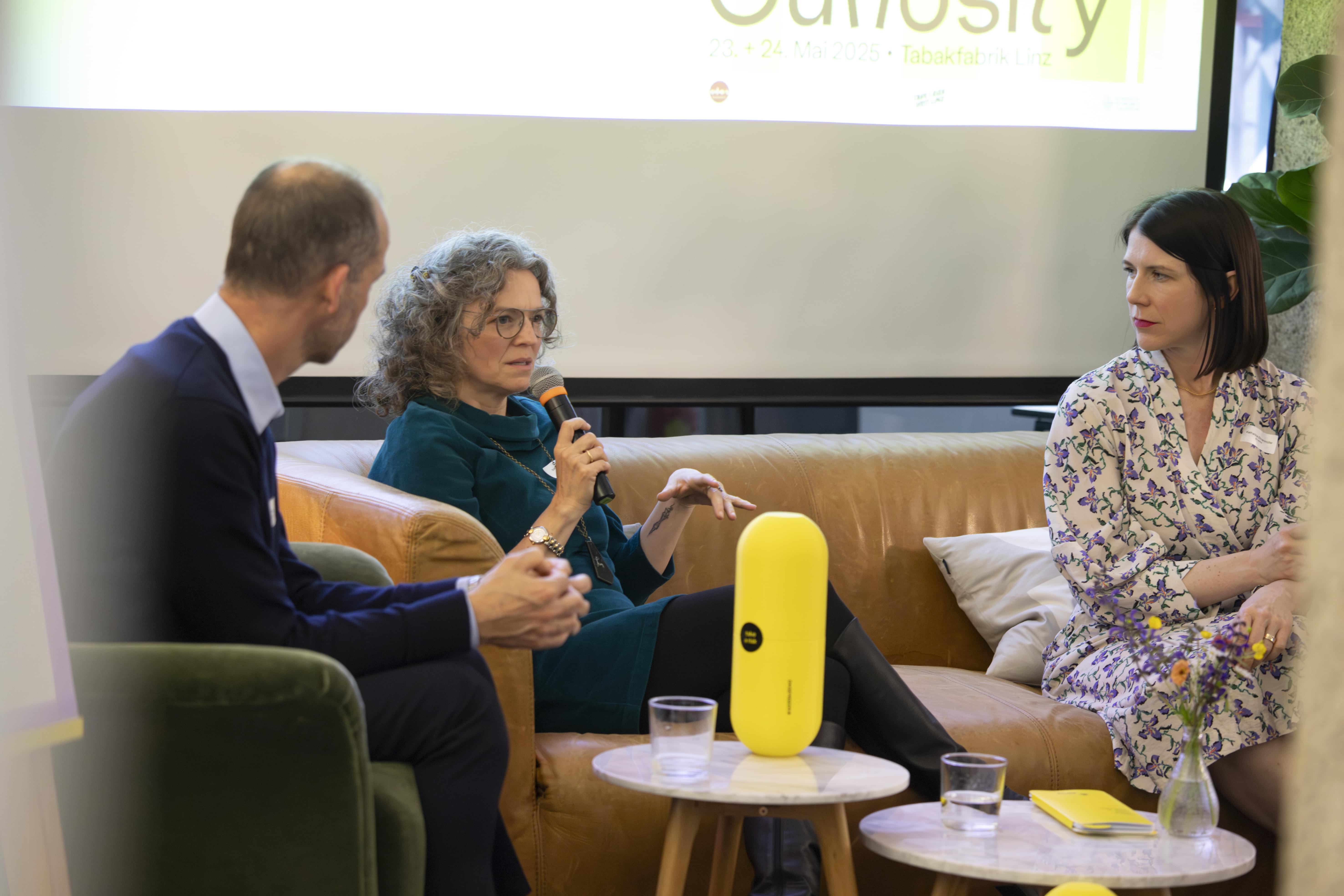 Drei Personen diskutieren auf einer Bühne bei der HR Coworking Night, eine Frau spricht ins Mikrofon.